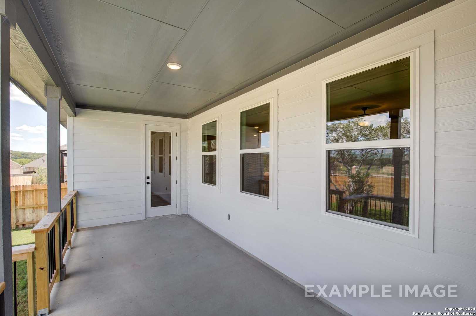 Covered back patio with large windows, white door, and wooden railing in Davidson Homes The Rockford G, Ladera, San Antonio