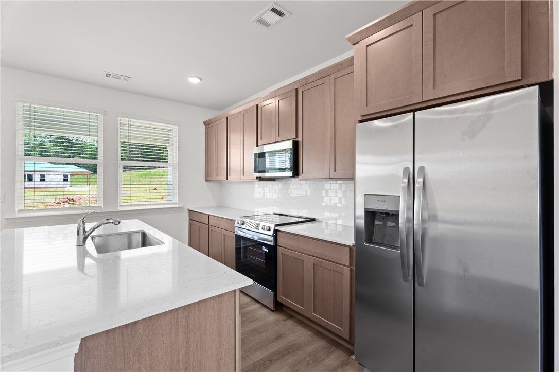 Modern kitchen with stainless appliances, white countertops, and wood cabinets in The Stella D home at Silver Oak, Cusseta.