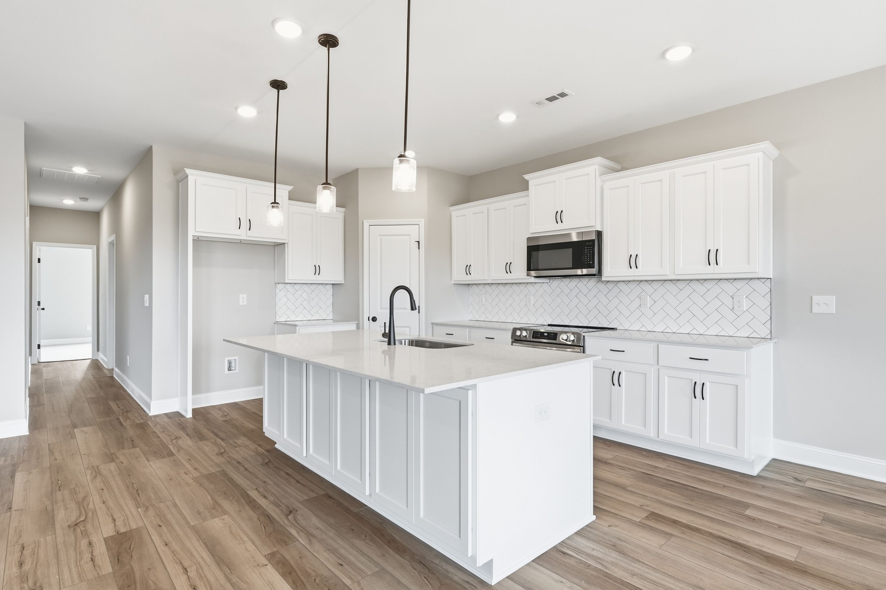 Spacious white kitchen in The Rockford home with large quartz island, shaker cabinets, subway tile backsplash, and pendant lights