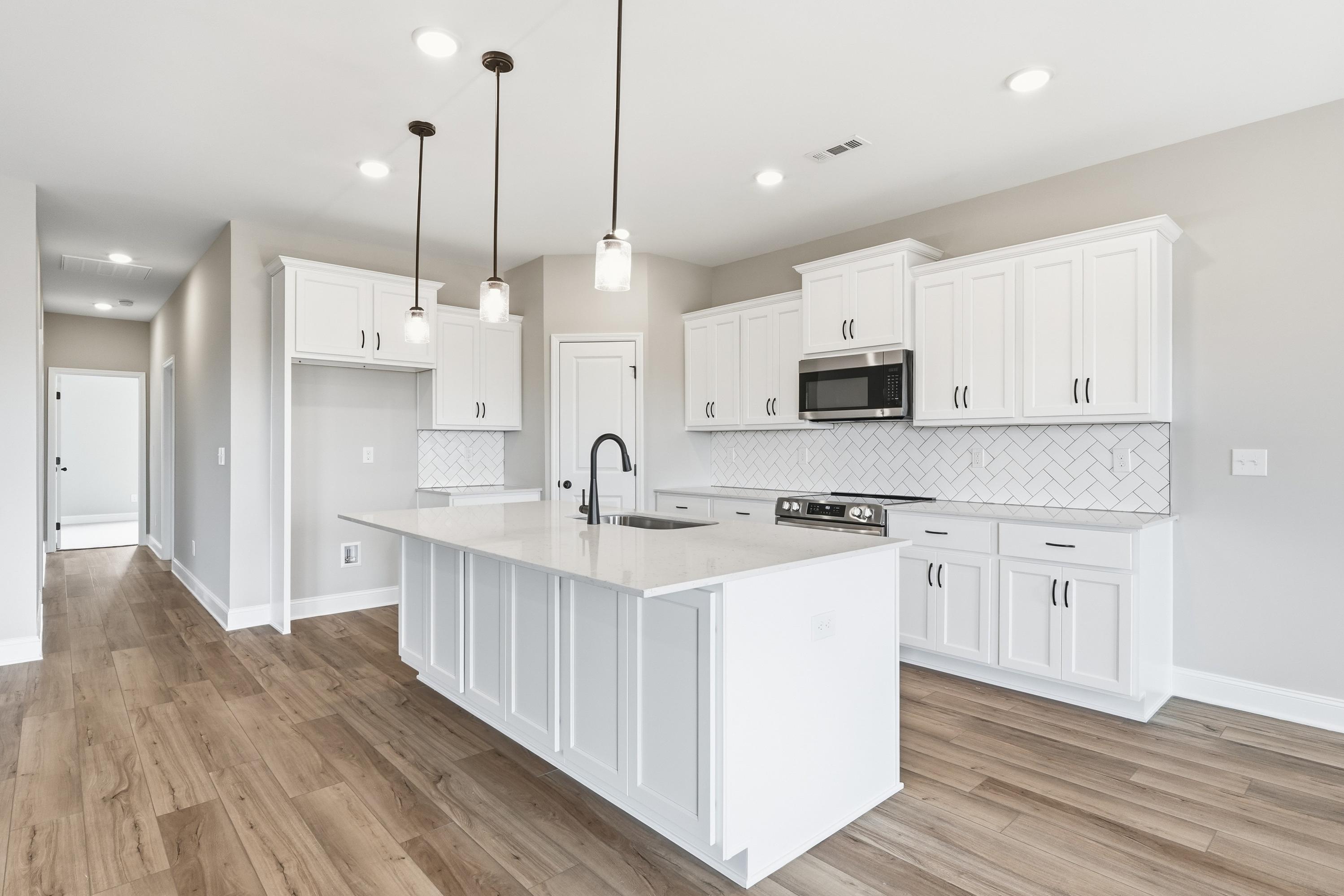 Spacious white kitchen in The Rockford home with large quartz island, shaker cabinets, subway tile backsplash, and pendant lights