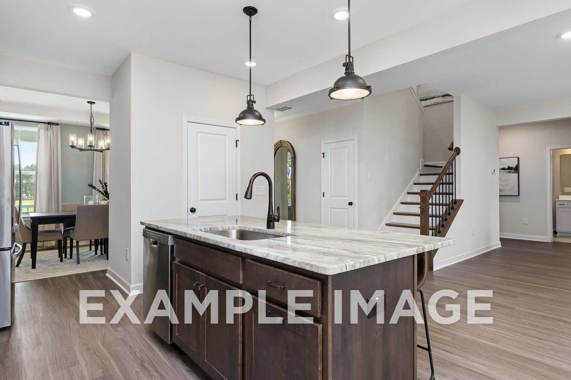 Spacious open-concept kitchen in The Willow with quartz island, pendant lights, dining area and staircase