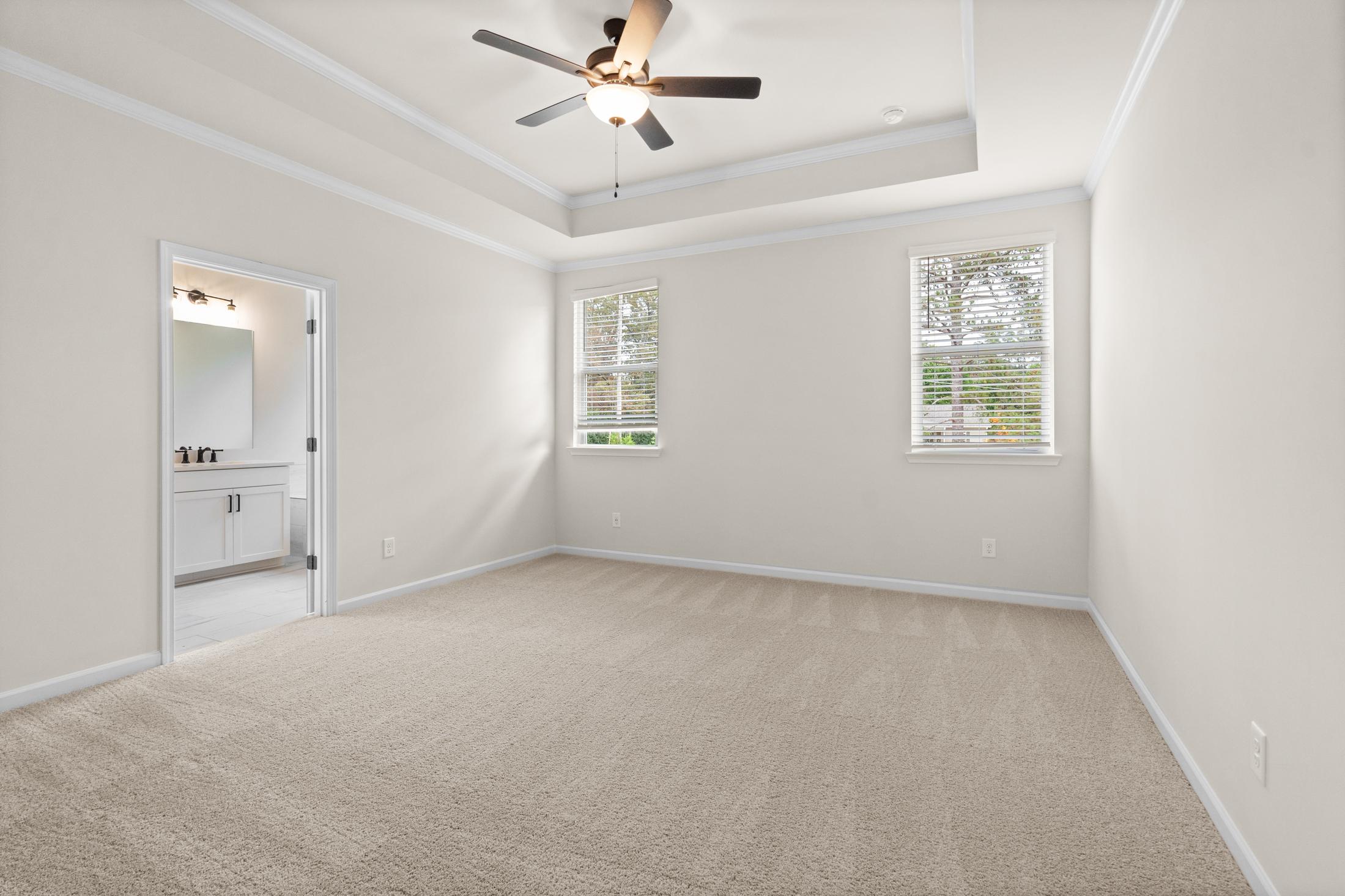 Spacious master bedroom in The Glenwood showcasing neutral walls, plush carpet, ceiling fan, large windows, and en-suite bath