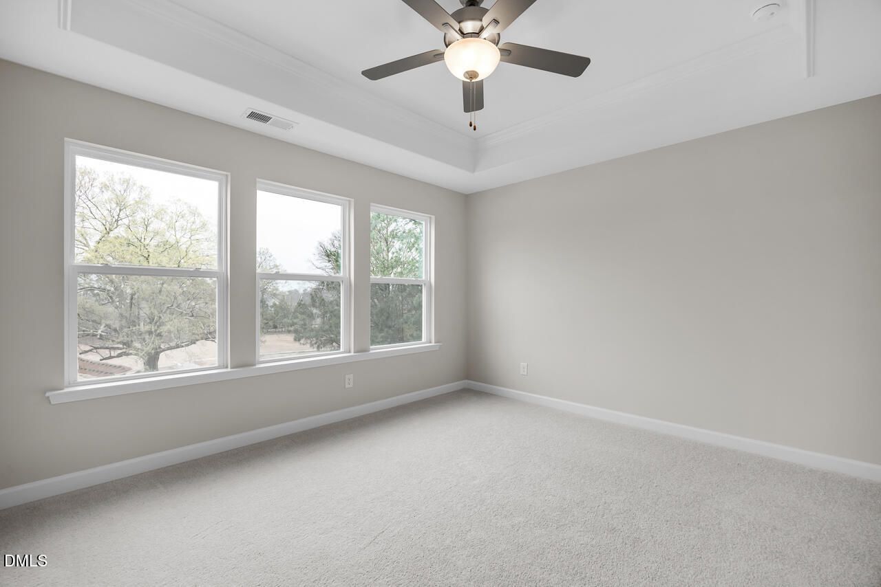 Spacious empty bedroom with large windows, trees view, ceiling fan, gray walls, beige carpet in Davidson Homes The Avery, Knightdale NC