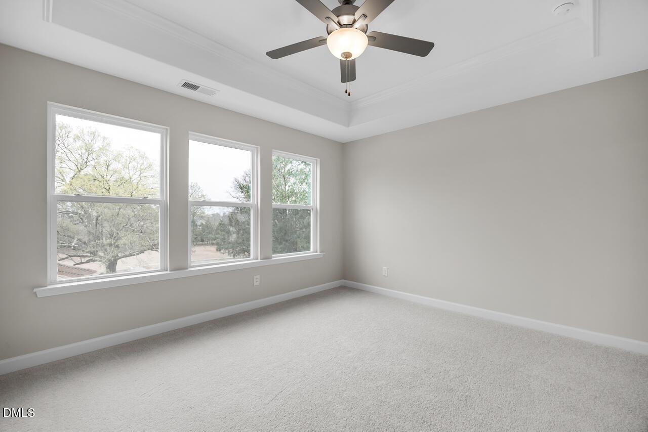 Spacious empty bedroom with large windows, trees view, ceiling fan, gray walls, beige carpet in Davidson Homes The Avery, Knightdale NC