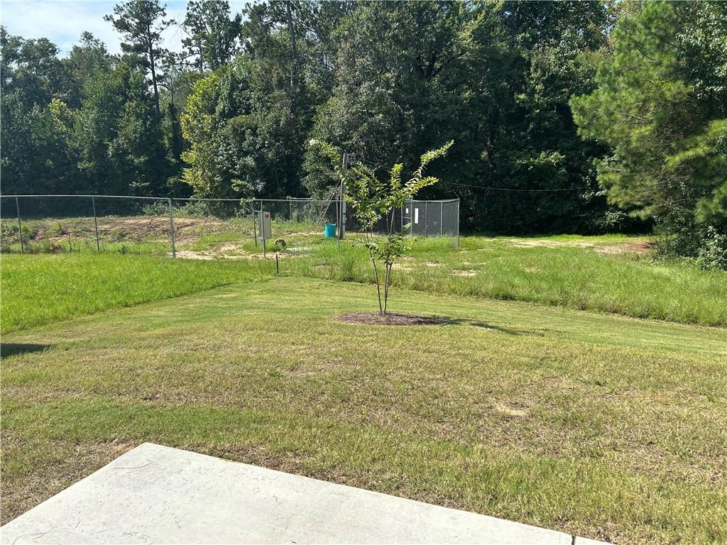 Spacious fenced backyard with lush grass, young tree, and surrounding pines in Davidson Homes The Washington, Phenix City, Alabama