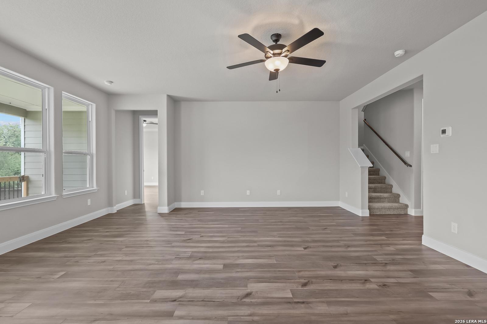 Spacious living room with gray walls, laminate wood floors, large windows to green view, ceiling fan in The Belmont H by Davidson Homes, Castroville, Texas