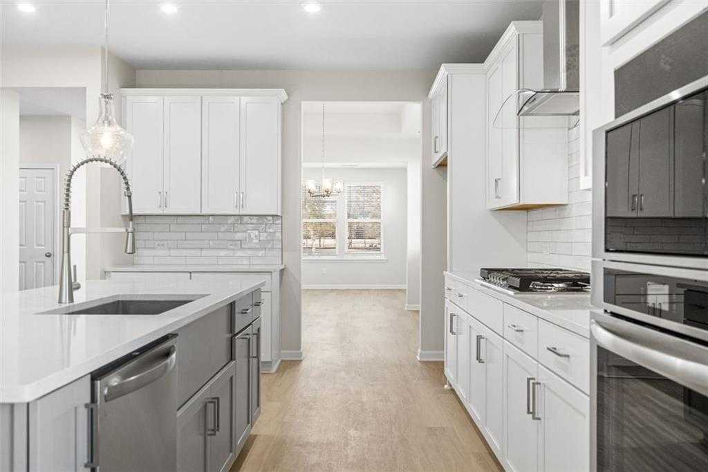 Modern open-concept kitchen with white shaker cabinets, gray island sink, stainless appliances in Davidson Homes The Glenwood C at Wehunt Meadows, Hoschton, GA