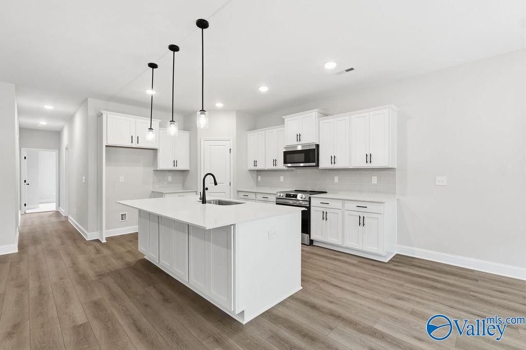 Modern white kitchen with quartz island, stainless steel appliances, and open layout in Davidson Homes The Rockford B, Hartselle, Alabama