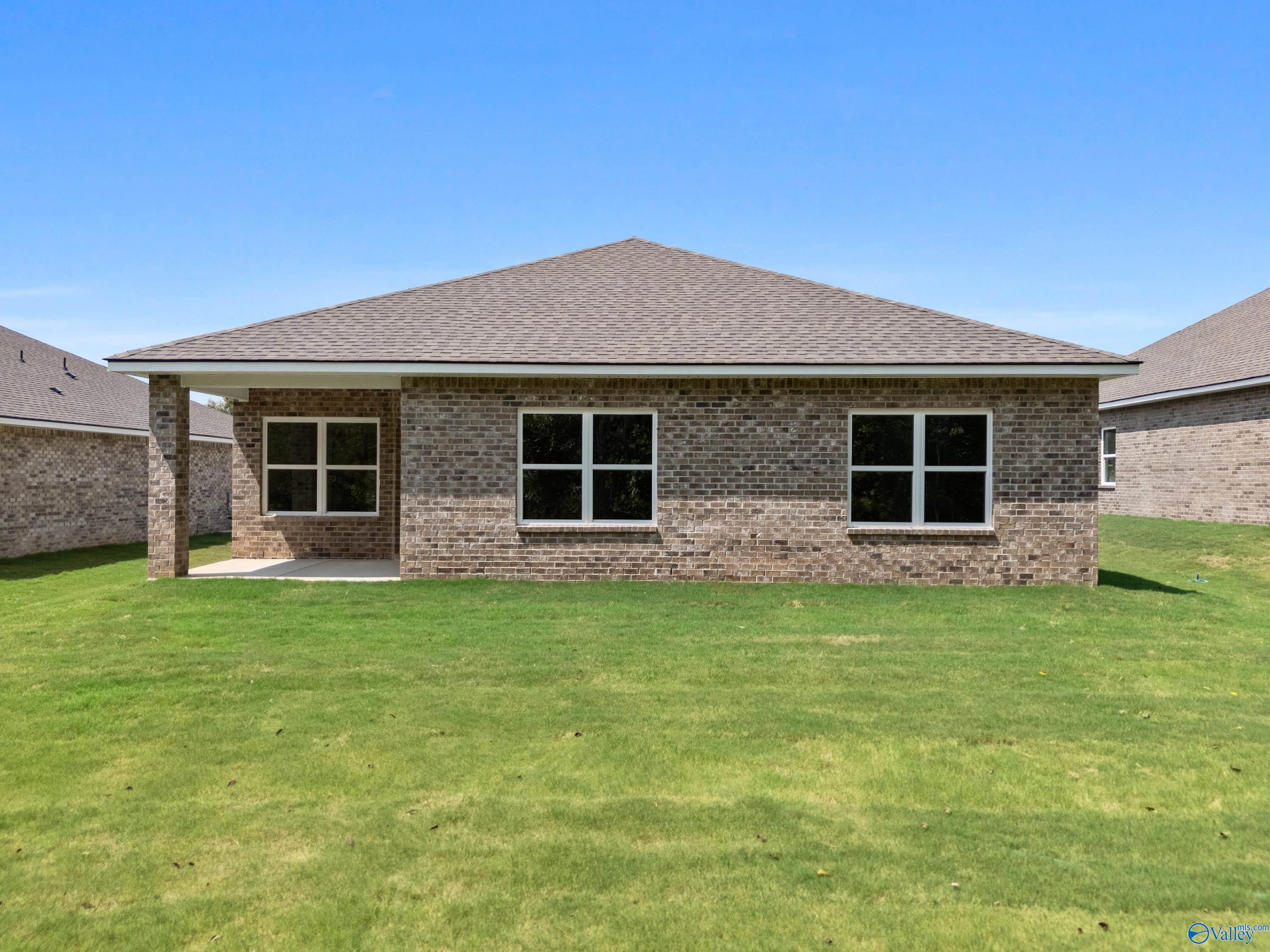 Rear view of The Daphne 1-story brick home with 2-car garage, covered patio, and lush green lawn in Spragins Cove, Huntsville, Alabama