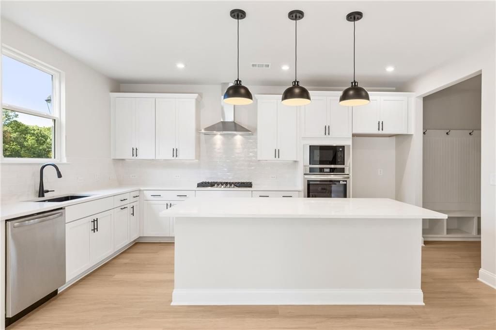 Modern white kitchen with large island, stainless appliances, and black pendants in The Hickory B by Davidson Homes, Buford, GA