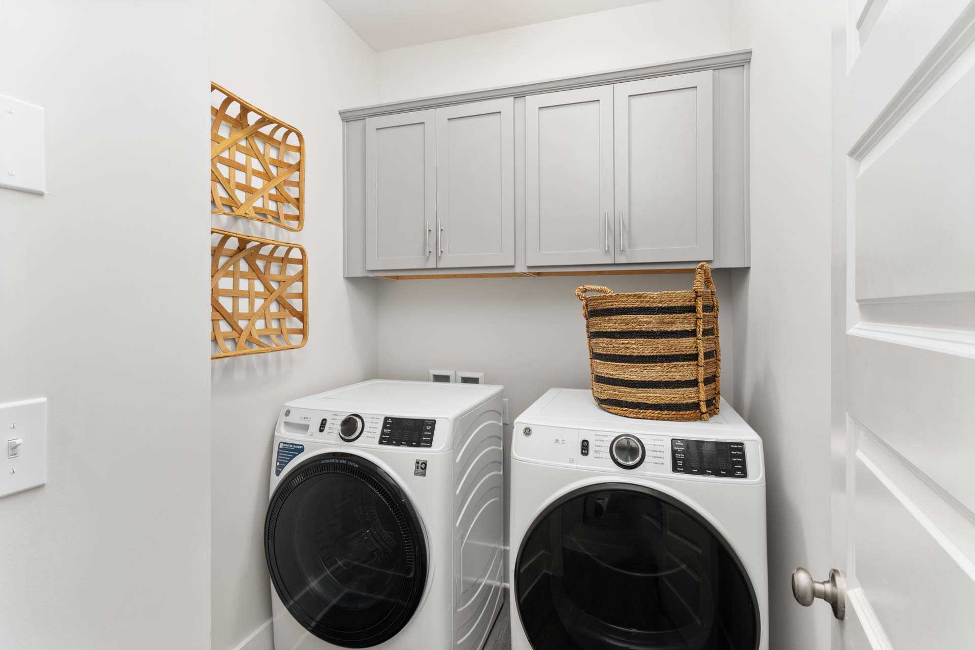 Spacious laundry room at The Meadows in Athens Alabama with white front-load washers dryers gray shaker cabinets wicker baskets