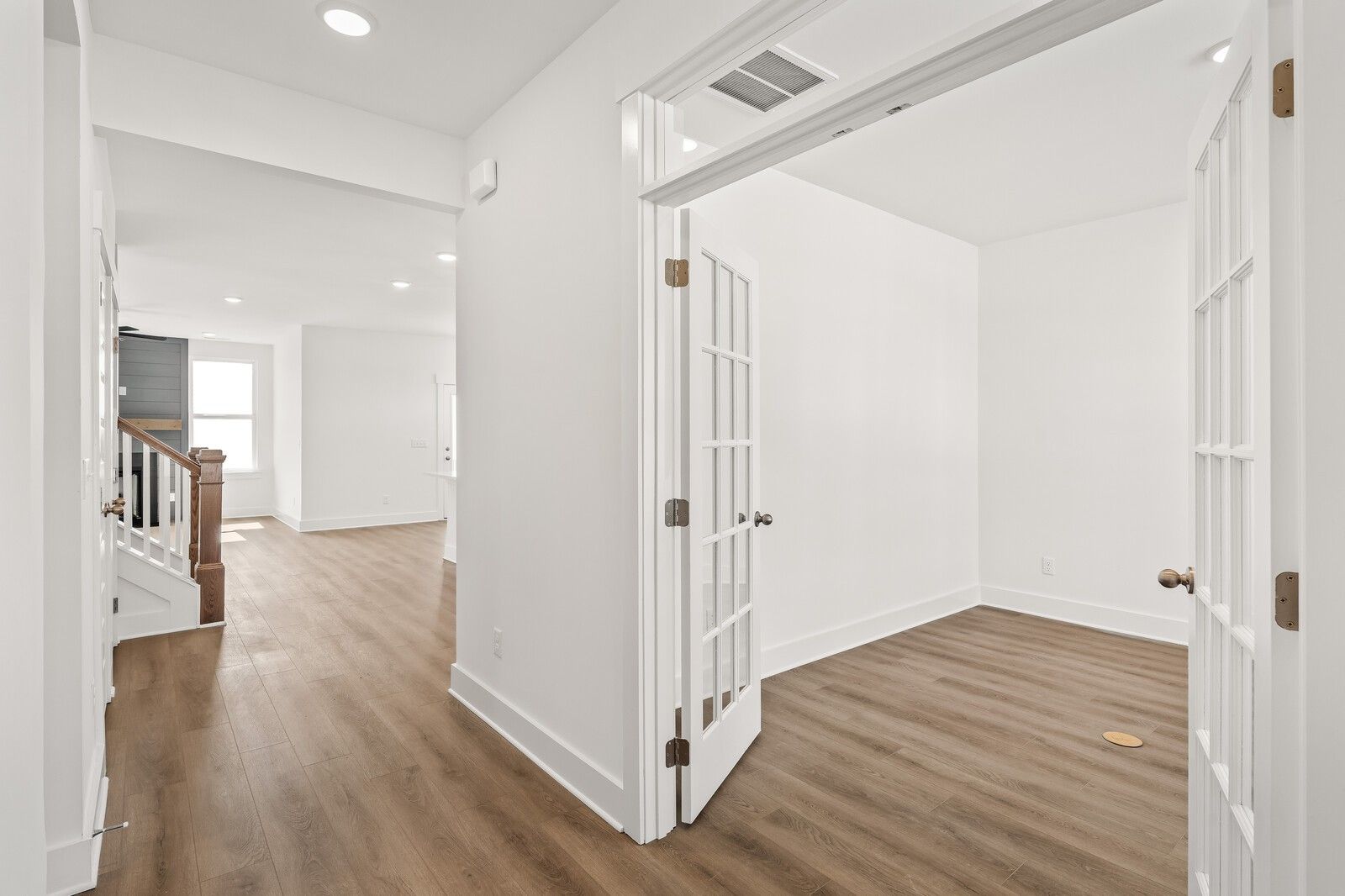 Bright hallway with open French doors to white study, hardwood floors, and wooden staircase in Davidson Homes The Ash A, Gallatin, TN