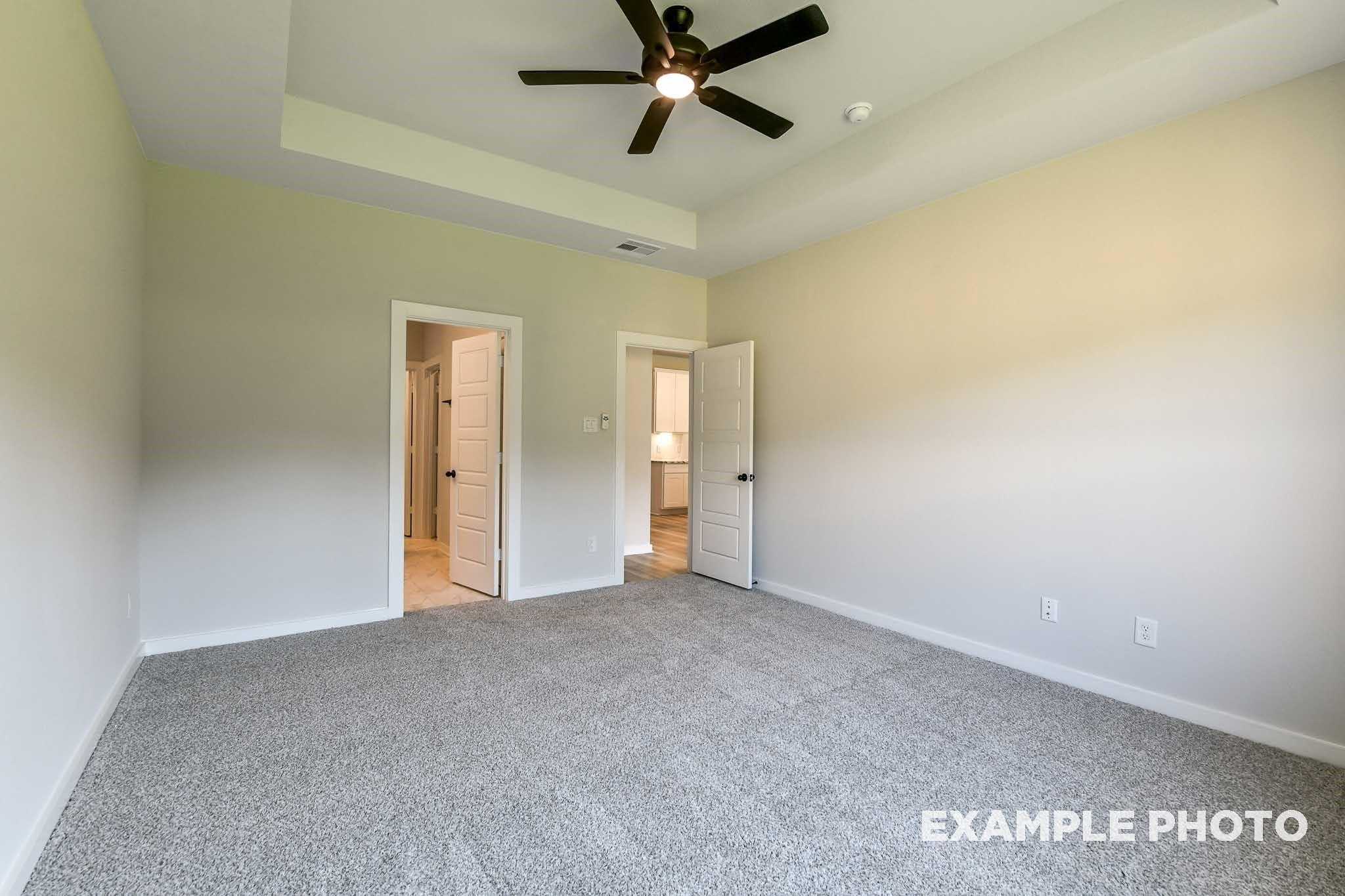 Spacious secondary bedroom featuring ceiling fan, beige walls, gray carpet, and en-suite bathroom in Davidson Homes The Everett C, Crosby, Texas
