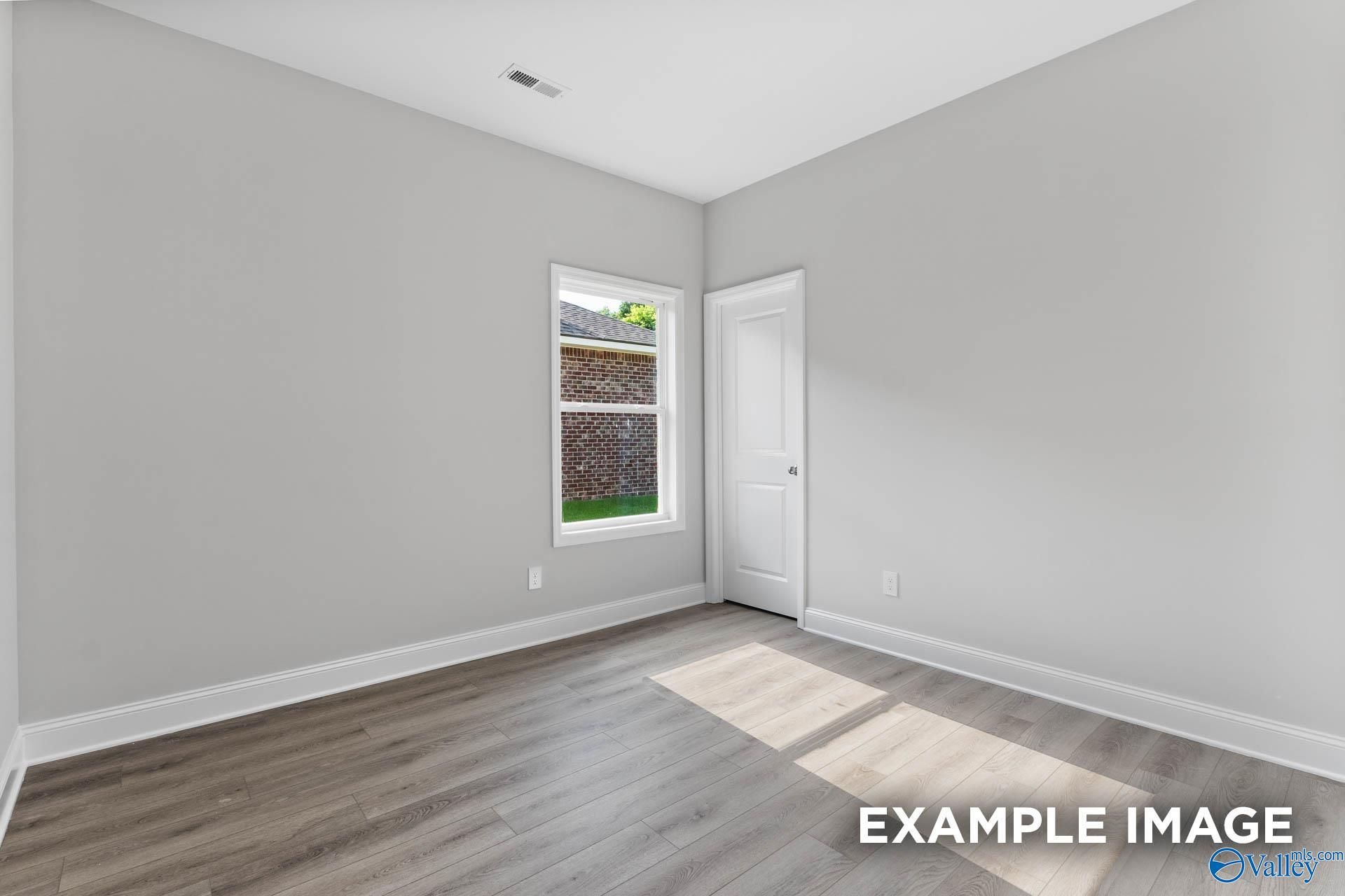 Bright bedroom featuring gray walls, luxury vinyl plank floors, and window overlooking backyard in Davidson Homes The Daphne C, Arab, Alabama