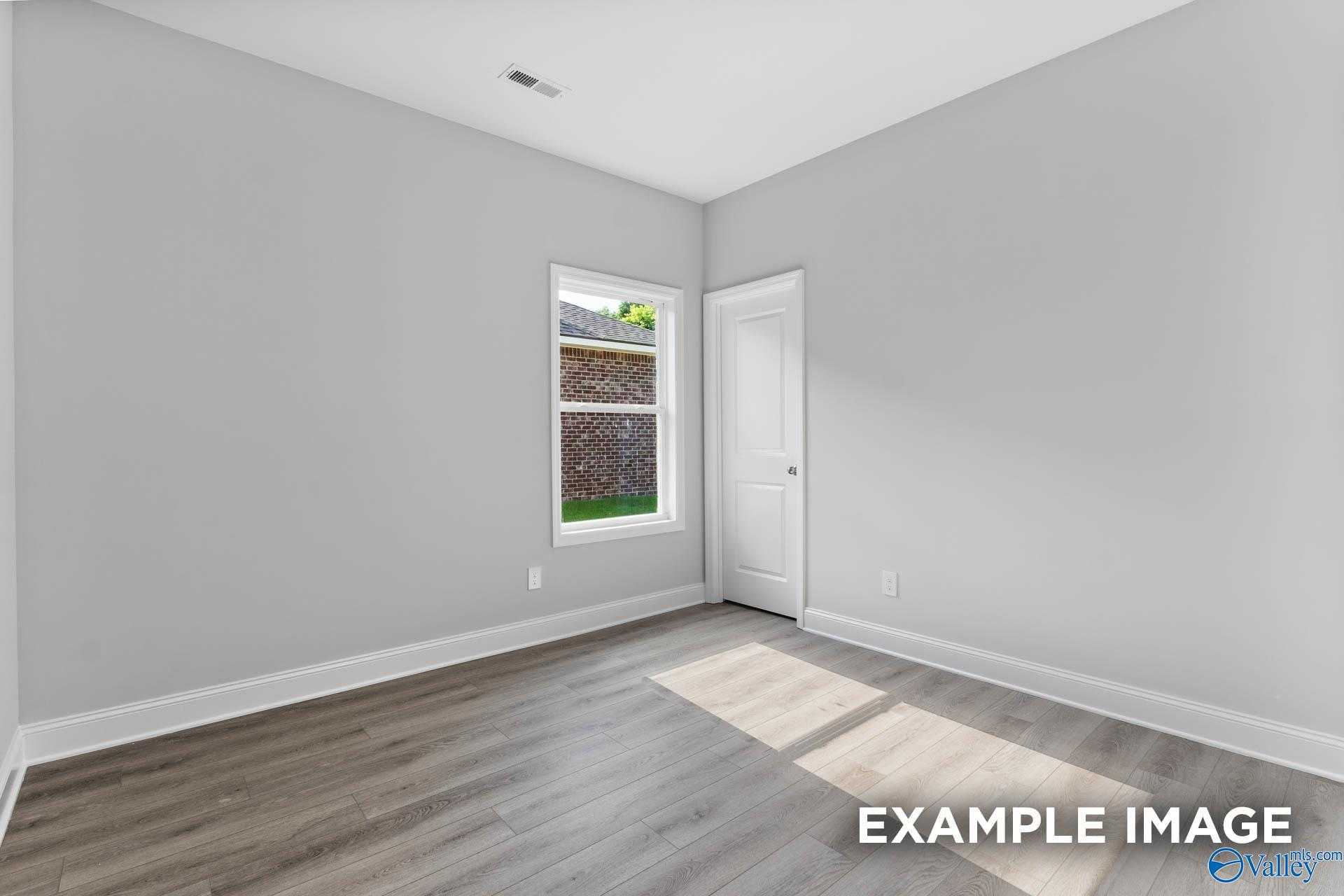 Bright bedroom featuring gray walls, luxury vinyl plank floors, and window overlooking backyard in Davidson Homes The Daphne C, Arab, Alabama