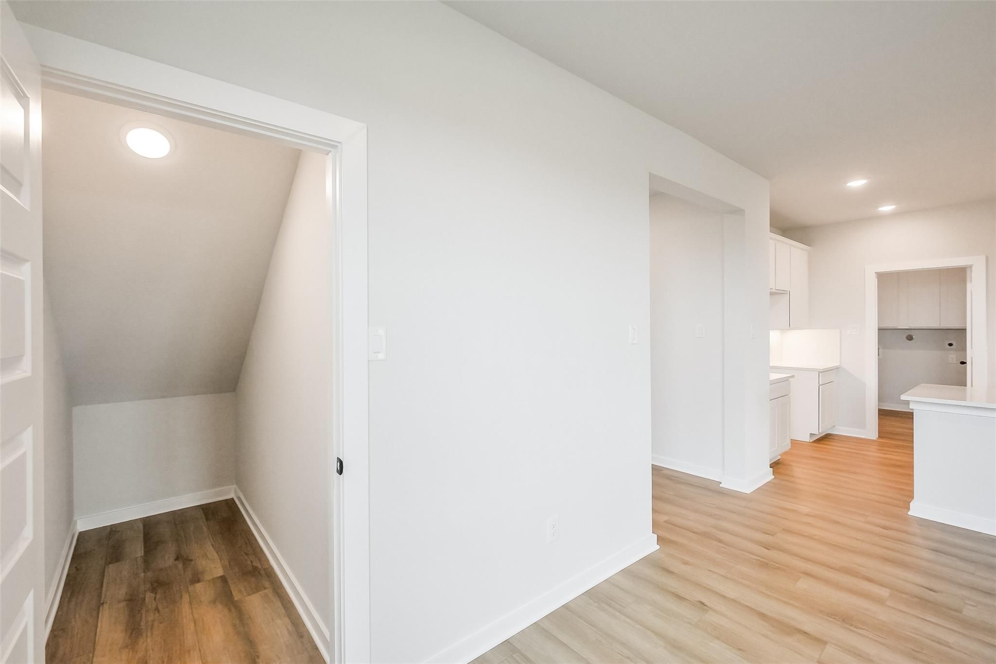 Elegant two-story staircase with light oak floors and open kitchen in Davidson Homes The Tierra B, Emberly, Beasley, Texas
