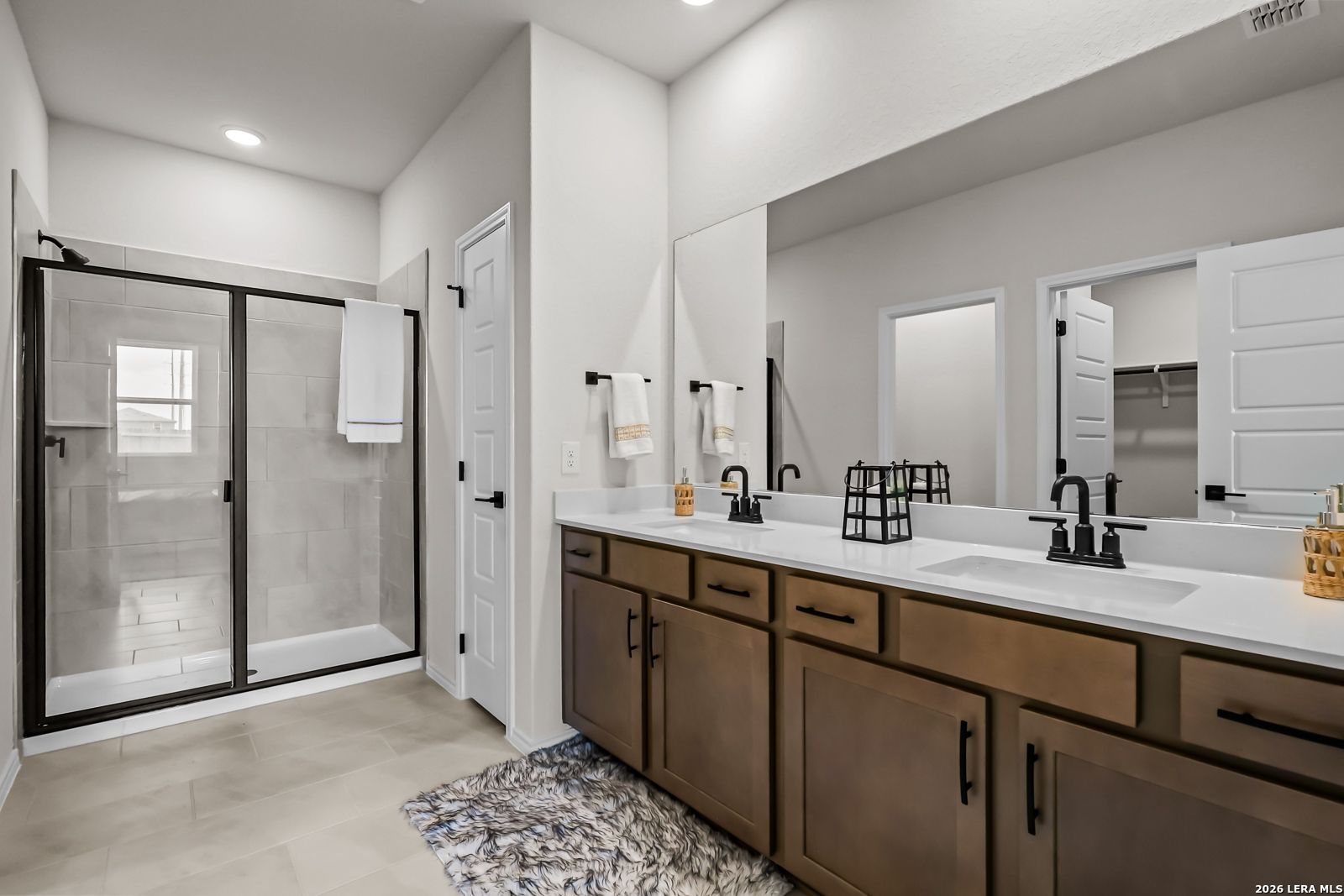 Modern primary bathroom with double vanity, walk-in shower, and walk-in closet in The Douglas C home in Seguin, Texas.