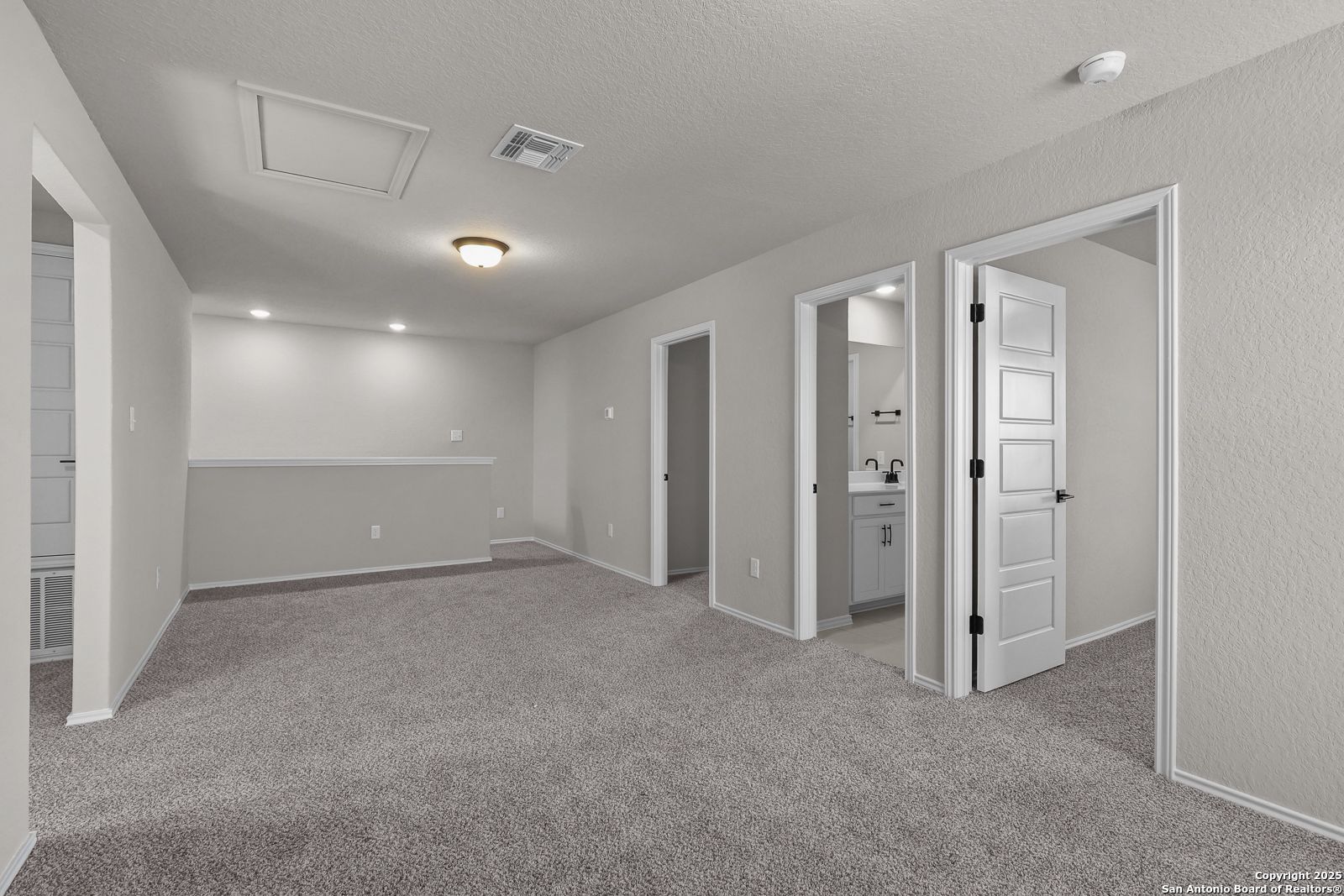 Upstairs hallway with gray carpet, open bedroom doors, and bathroom vanity in 5-bedroom The Brazos C home, San Antonio, TX