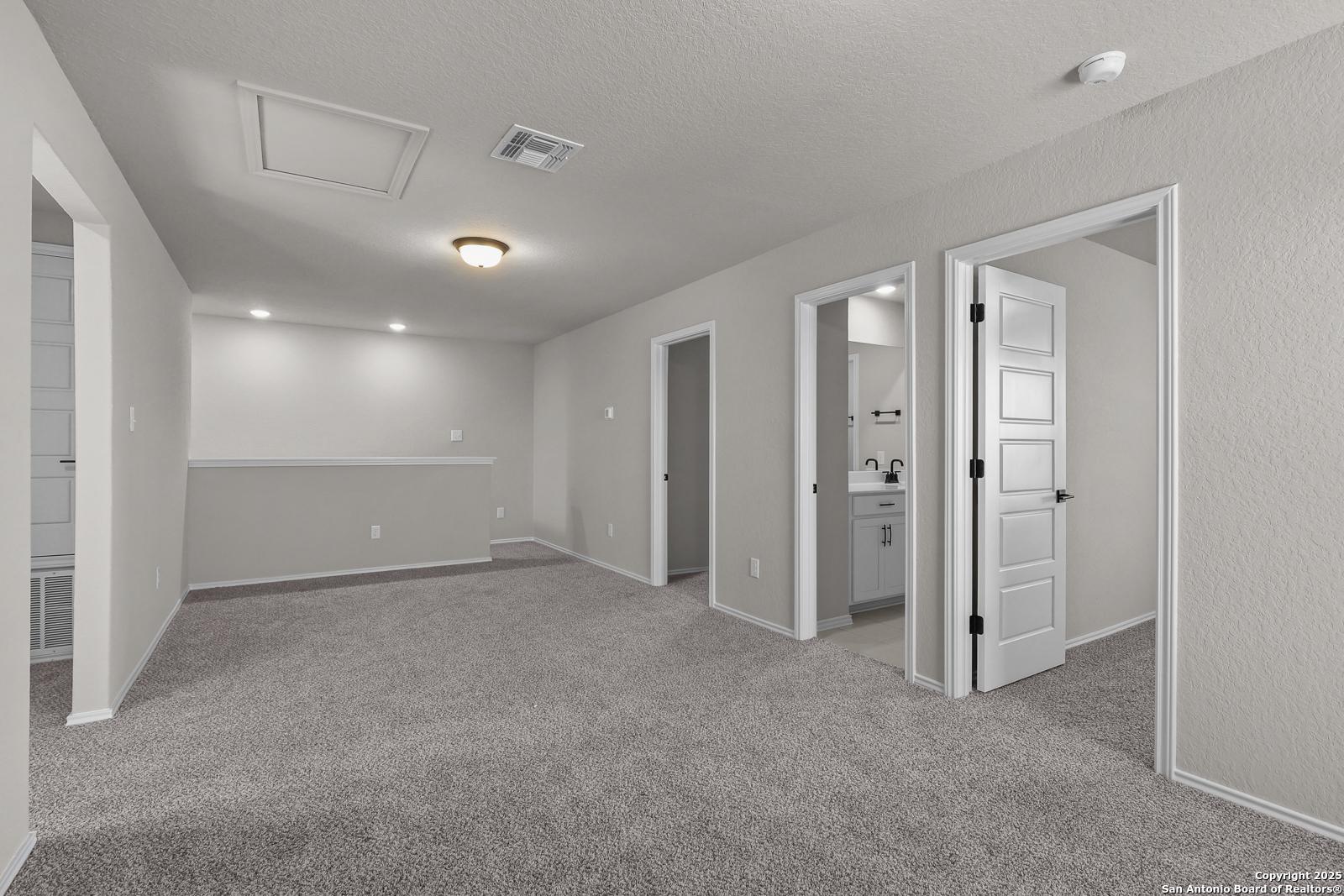 Upstairs hallway with gray carpet, open bedroom doors, and bathroom vanity in 5-bedroom The Brazos C home, San Antonio, TX
