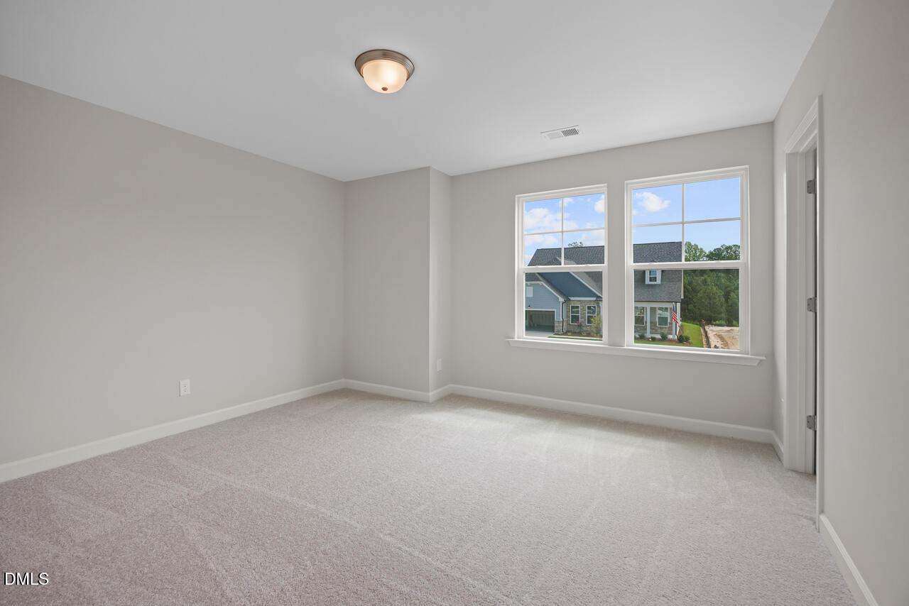 Bright secondary bedroom with plush carpet and large windows in The Chestnut floor plan at Wendell Ridge, North Carolina.