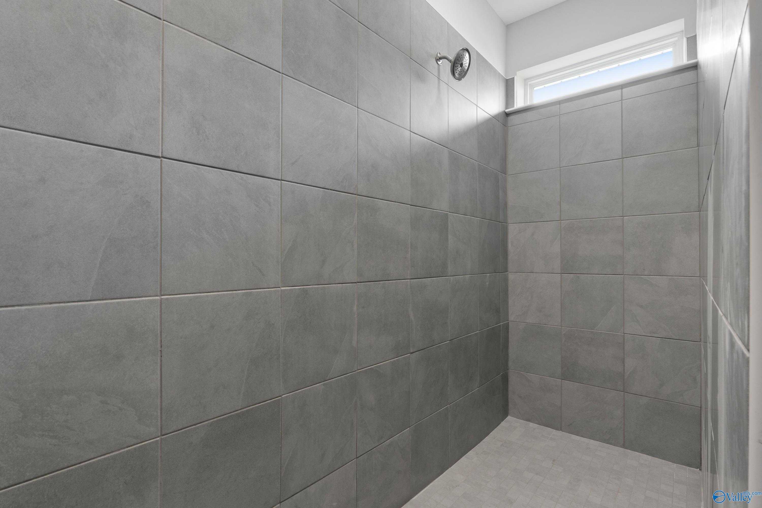 Elegant gray tiled walk-in shower with frameless enclosure and window in master bath of Davidson Homes The Dorado, Athens, Alabama