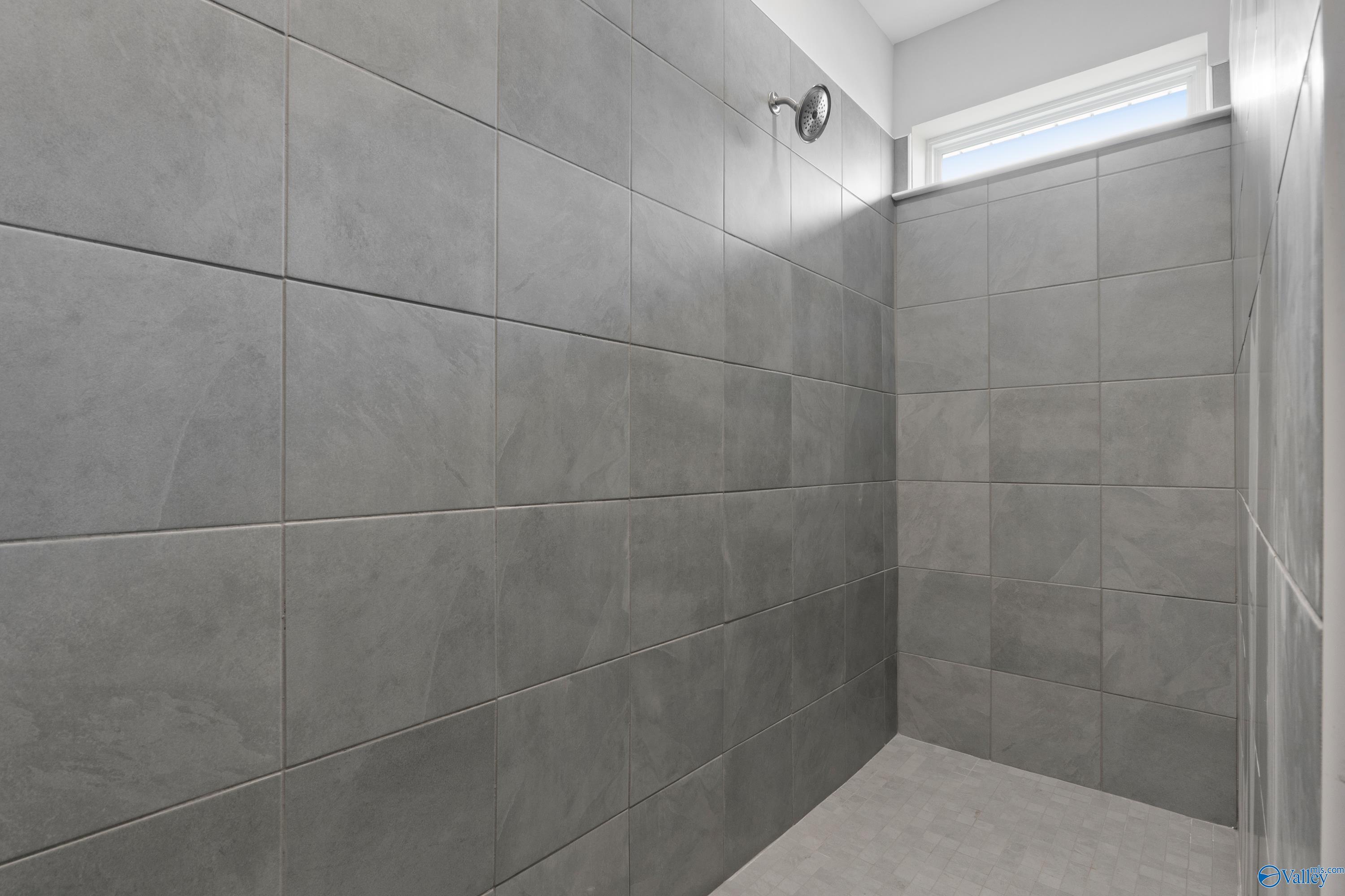 Elegant gray tiled walk-in shower with frameless enclosure and window in master bath of Davidson Homes The Dorado, Athens, Alabama