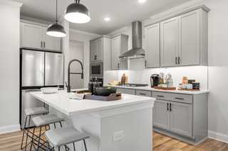 Gourmet kitchen in The Washington H townhome featuring gray shaker cabinets, white quartz island, bar stools, and stainless appliances