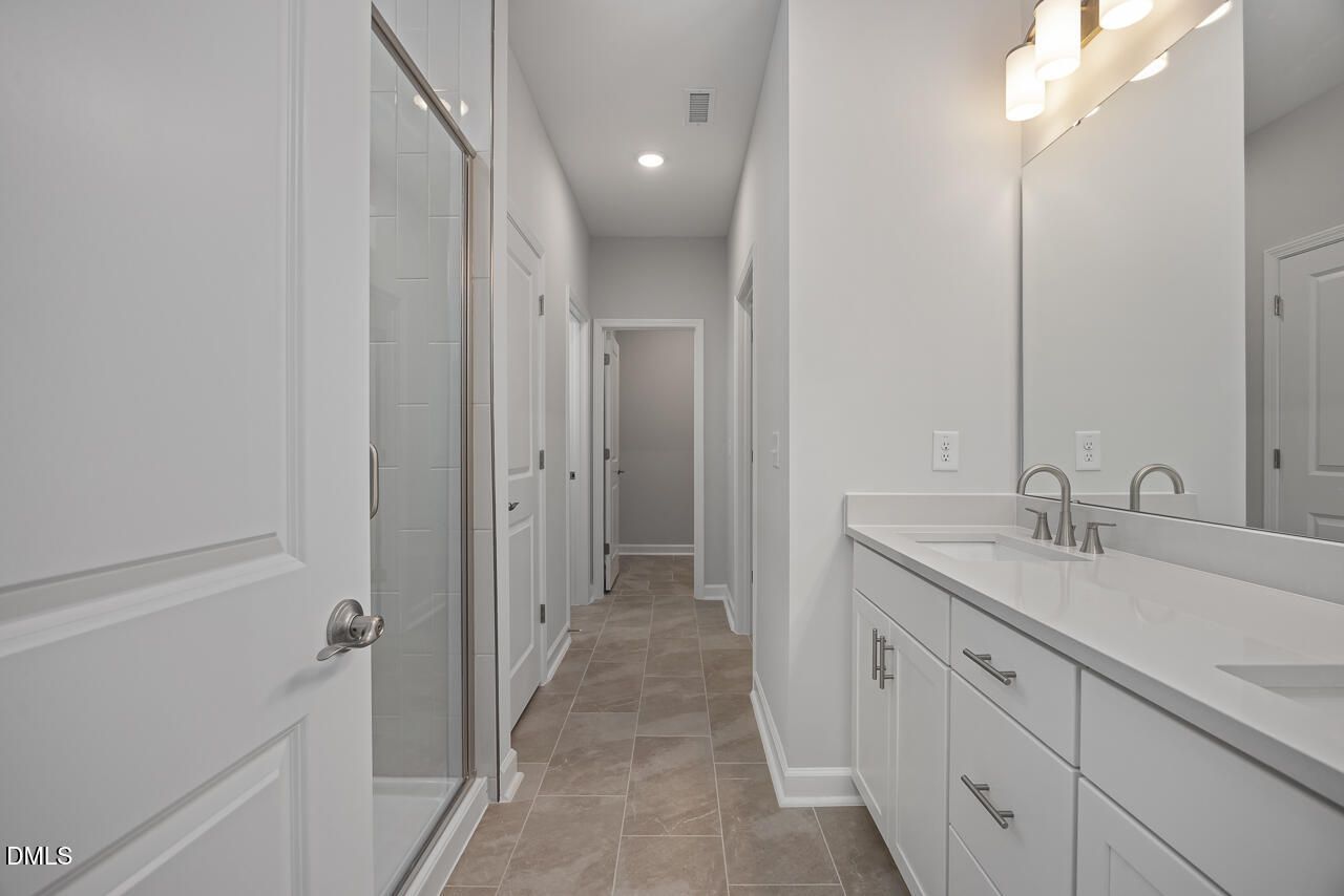 Modern bathroom with white dual vanity, tile flooring, and glass-enclosed shower in The Ashport L at Sage on North Main.