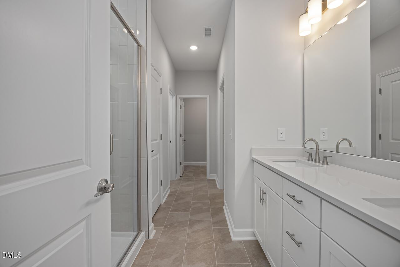Modern bathroom with white dual vanity, tile flooring, and glass-enclosed shower in The Ashport L at Sage on North Main.