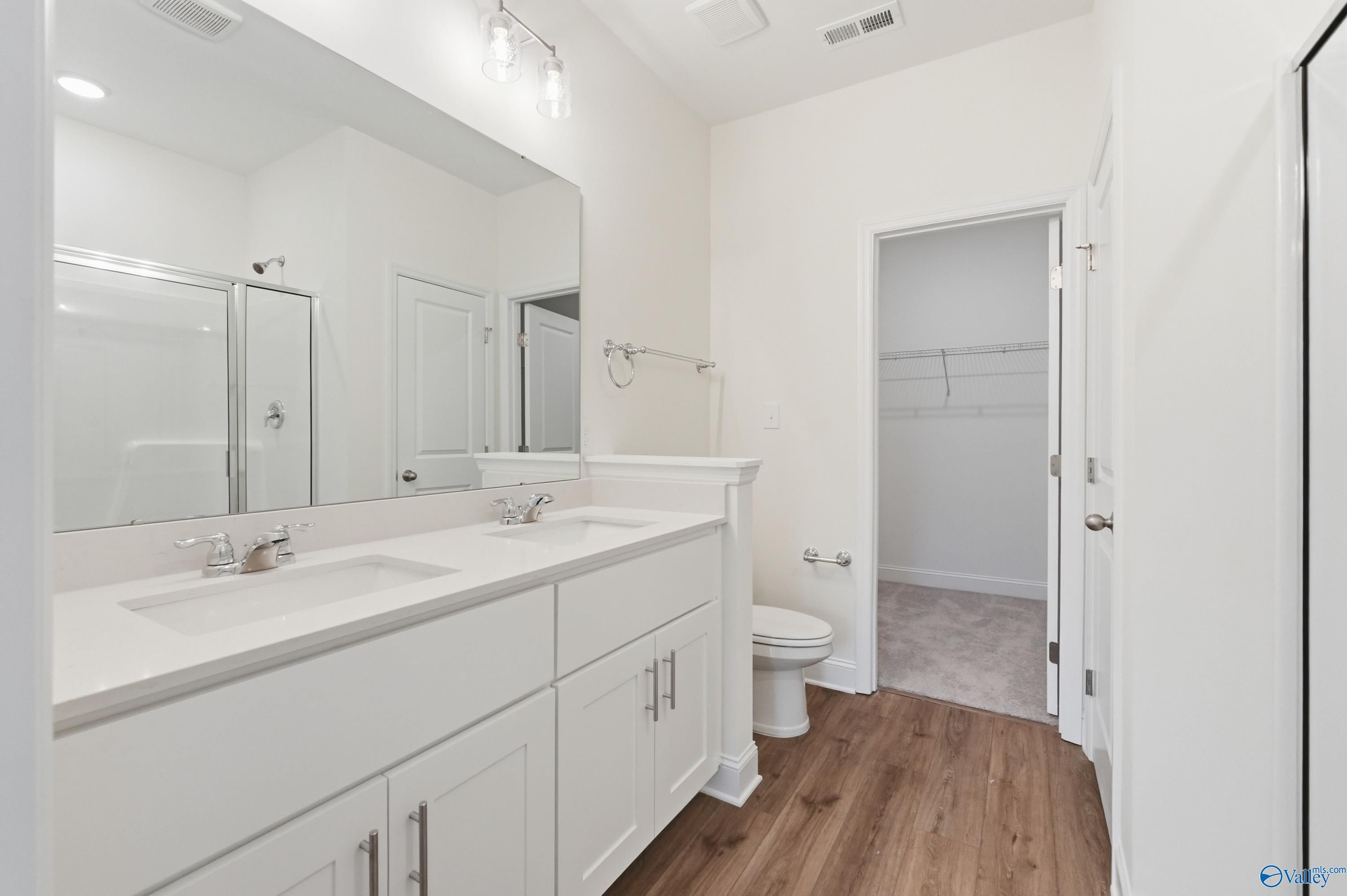 Modern master bathroom featuring double vanity, frameless glass shower, and wood floors in Davidson Homes Asheville C, Meridianville AL