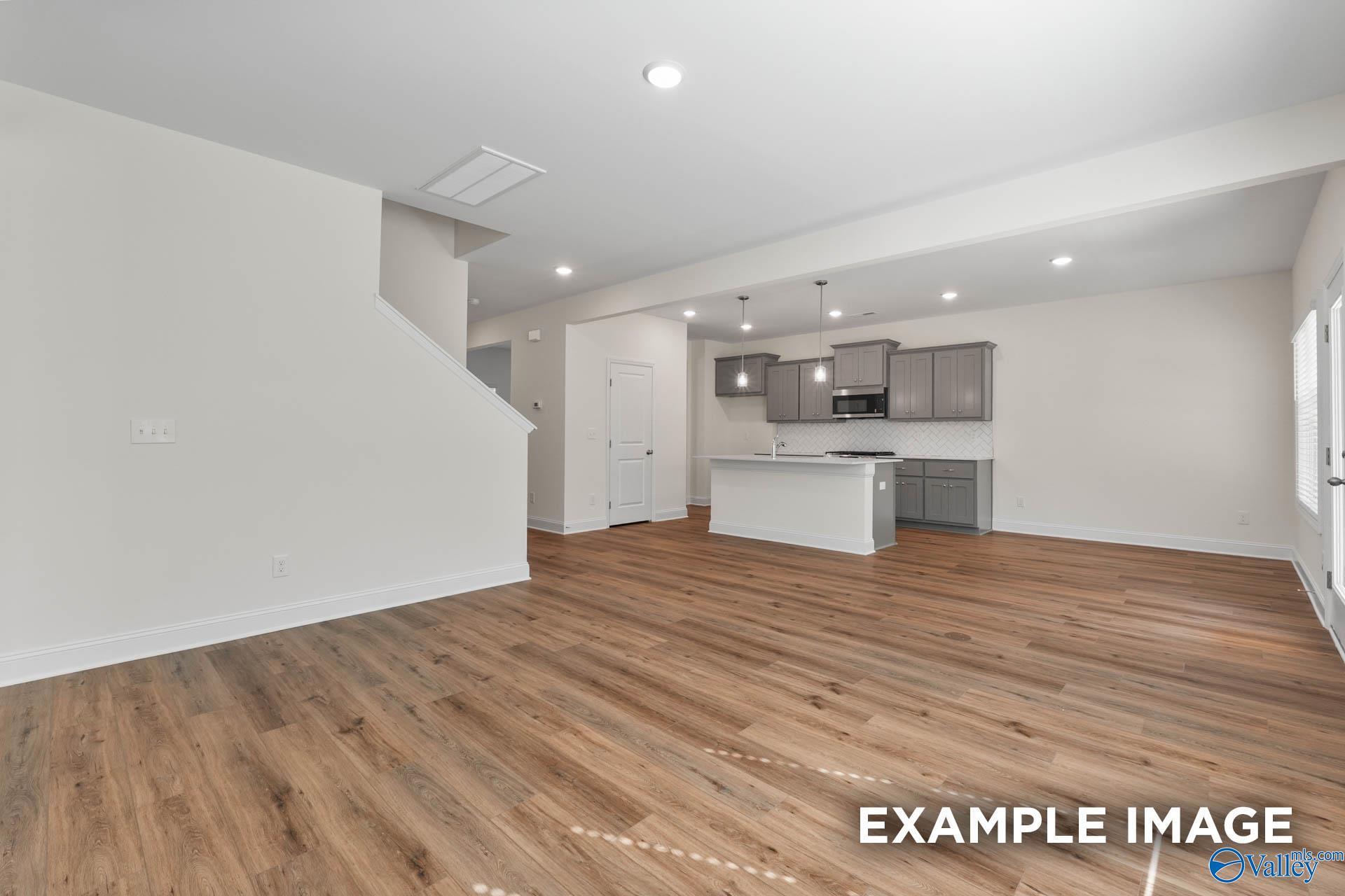 Modern open-concept kitchen with gray cabinets, white island, hardwood floors, and staircase in The Shelby A, Hazel Green, Alabama