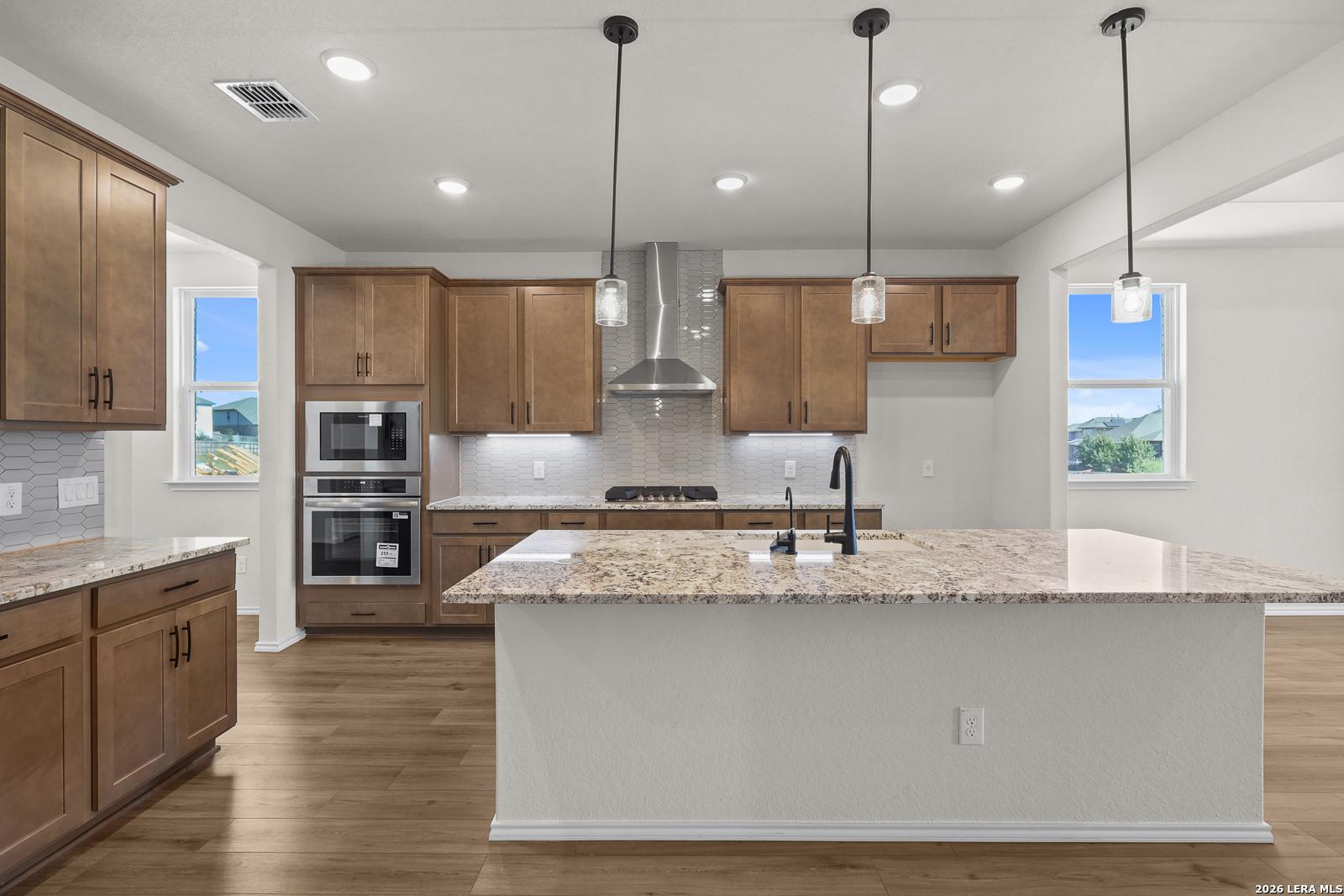 Kitchen island with granite countertops, pendant lights, and stainless appliances in Davidson Homes The Glenwood E, Comanche Ridge, San Antonio