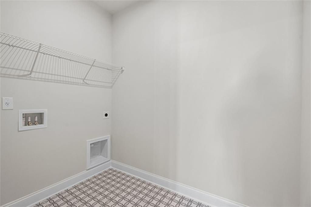 Spacious laundry room with wire shelving, washer-dryer hookups, and checkered tile floor in Davidson Homes The Ash C at Wehunt Meadows, Hoschton