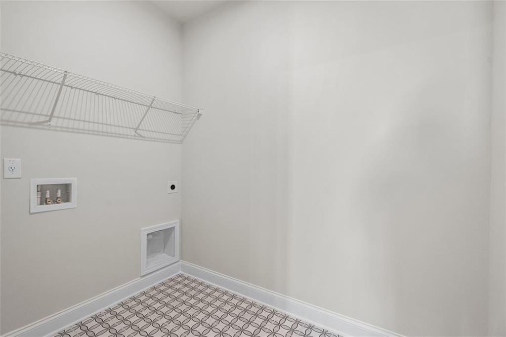 Spacious laundry room with wire shelving, washer-dryer hookups, and checkered tile floor in Davidson Homes The Ash C at Wehunt Meadows, Hoschton