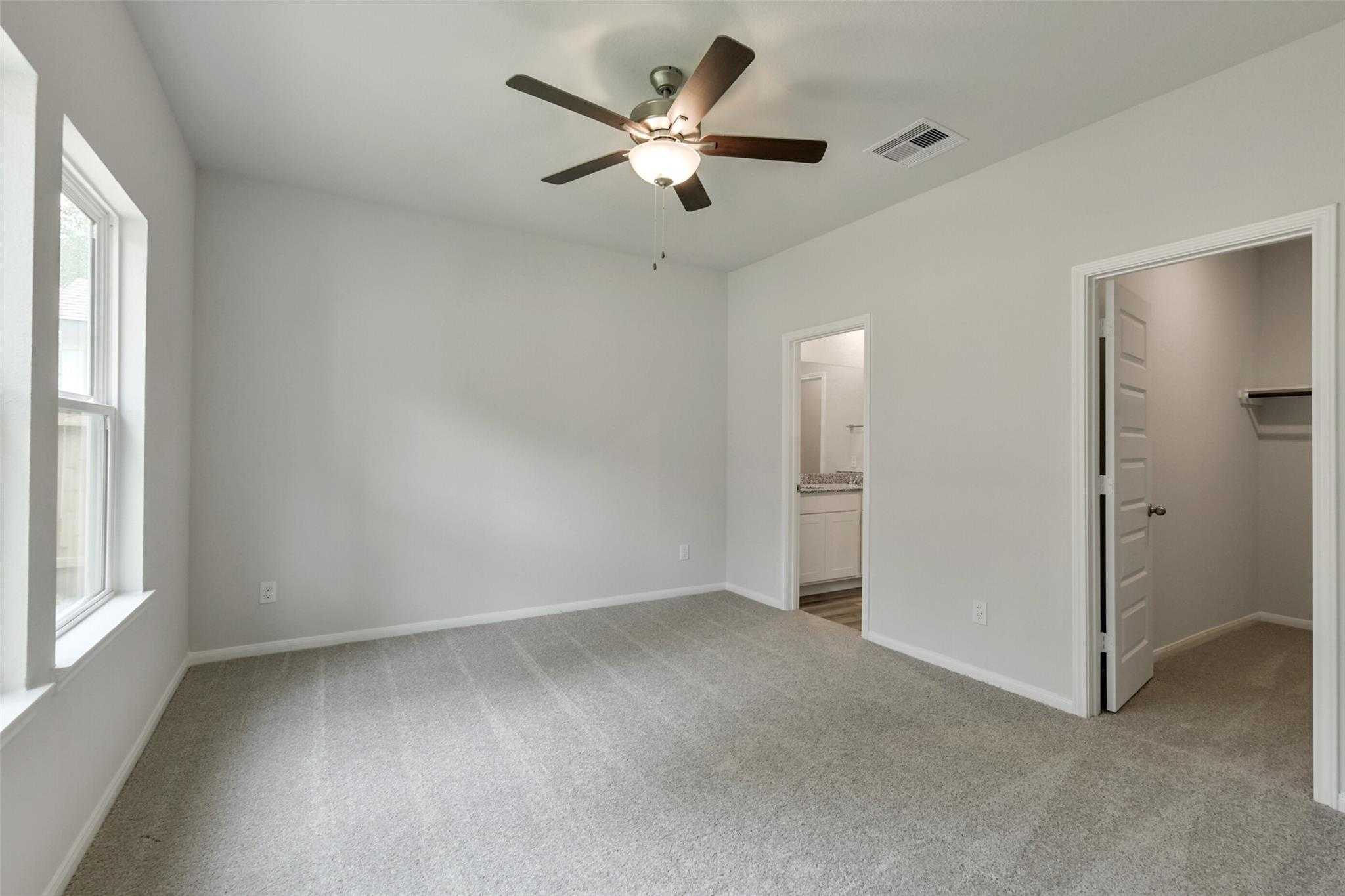 Bright bedroom with ceiling fan, carpet flooring, and en-suite bath in Davidson Homes The Frio G, Conroe, Texas