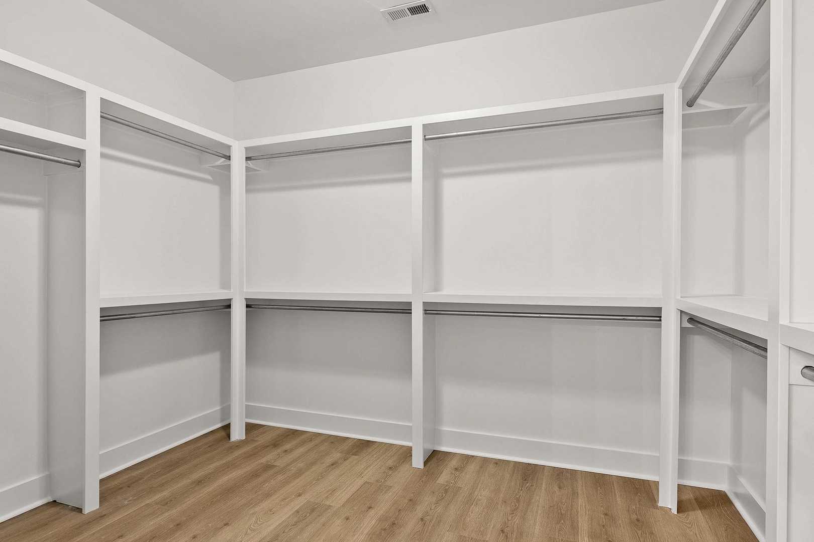 Spacious walk-in closet in The Oxford master suite with white built-in shelving, hanging rods, and hardwood flooring