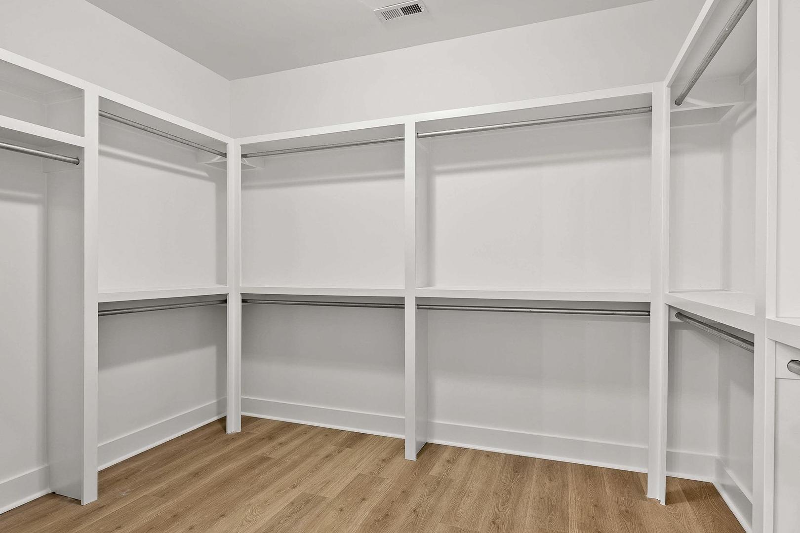 Spacious walk-in closet in The Oxford master suite with white built-in shelving, hanging rods, and hardwood flooring
