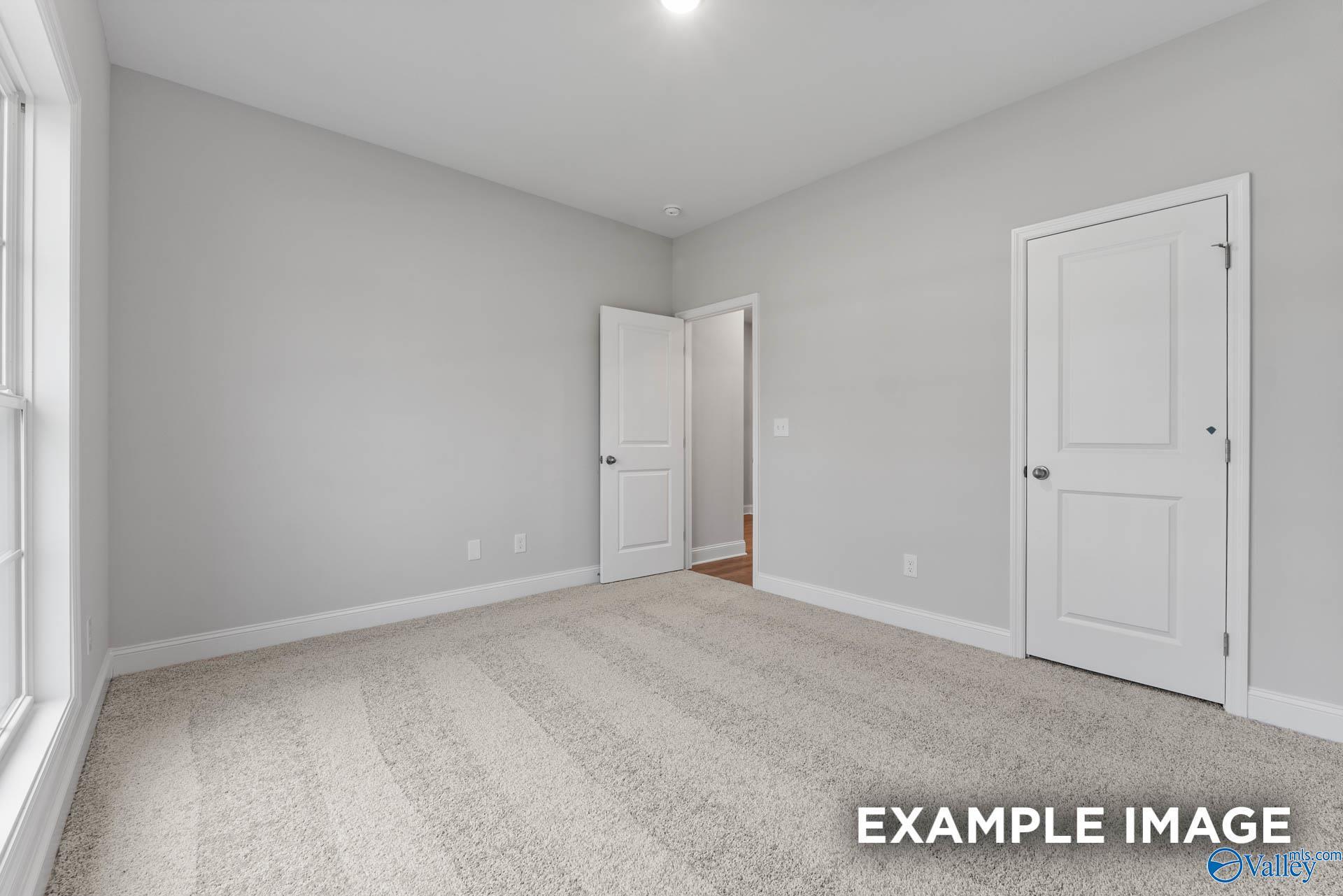 Spacious secondary bedroom with light gray walls, beige carpet, double doors, and large window in The Daphne home, Meridianville, AL