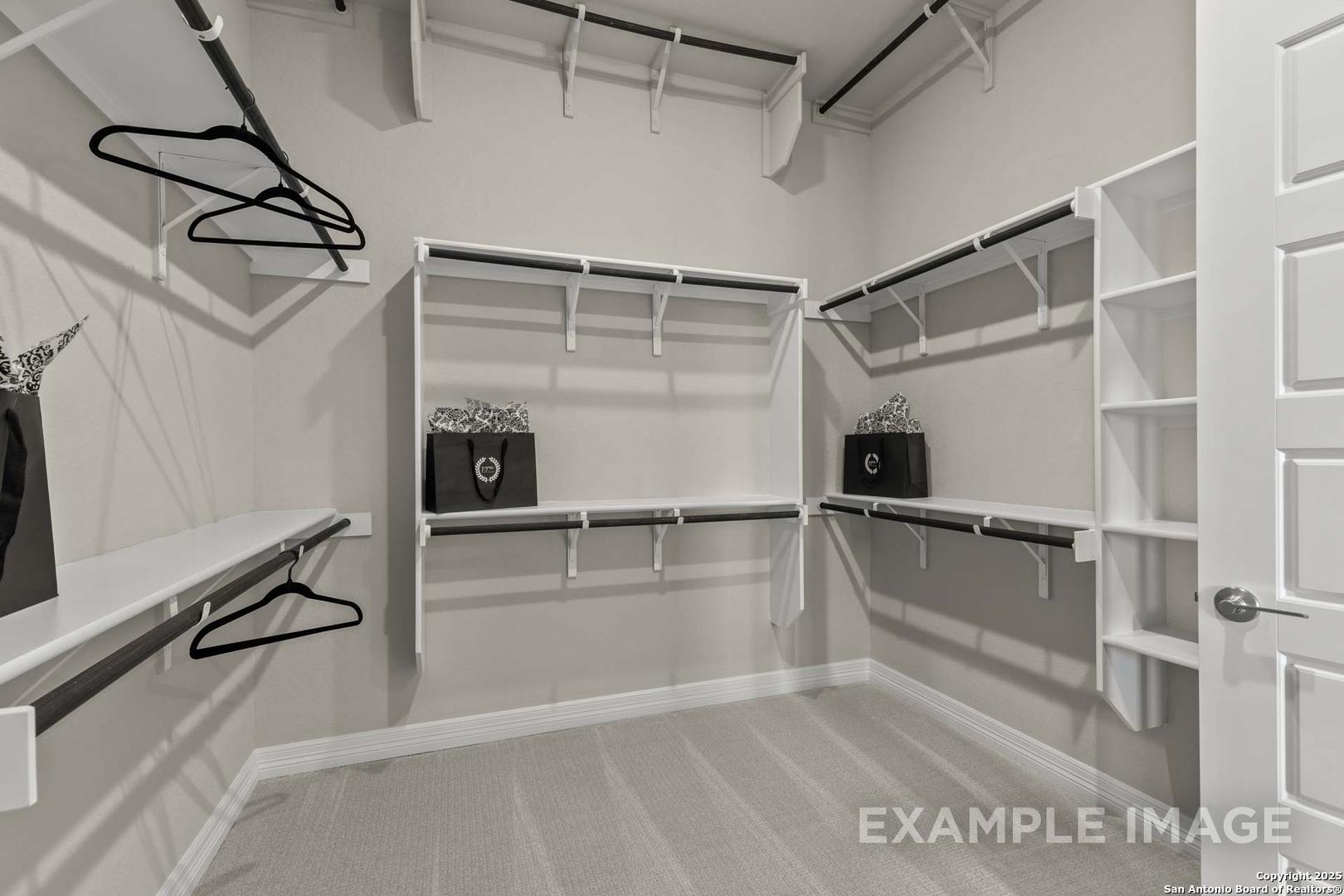 Spacious walk-in closet with built-in white shelving, hanging rods, and storage in Davidson Homes Summerlin B, Castroville, Texas