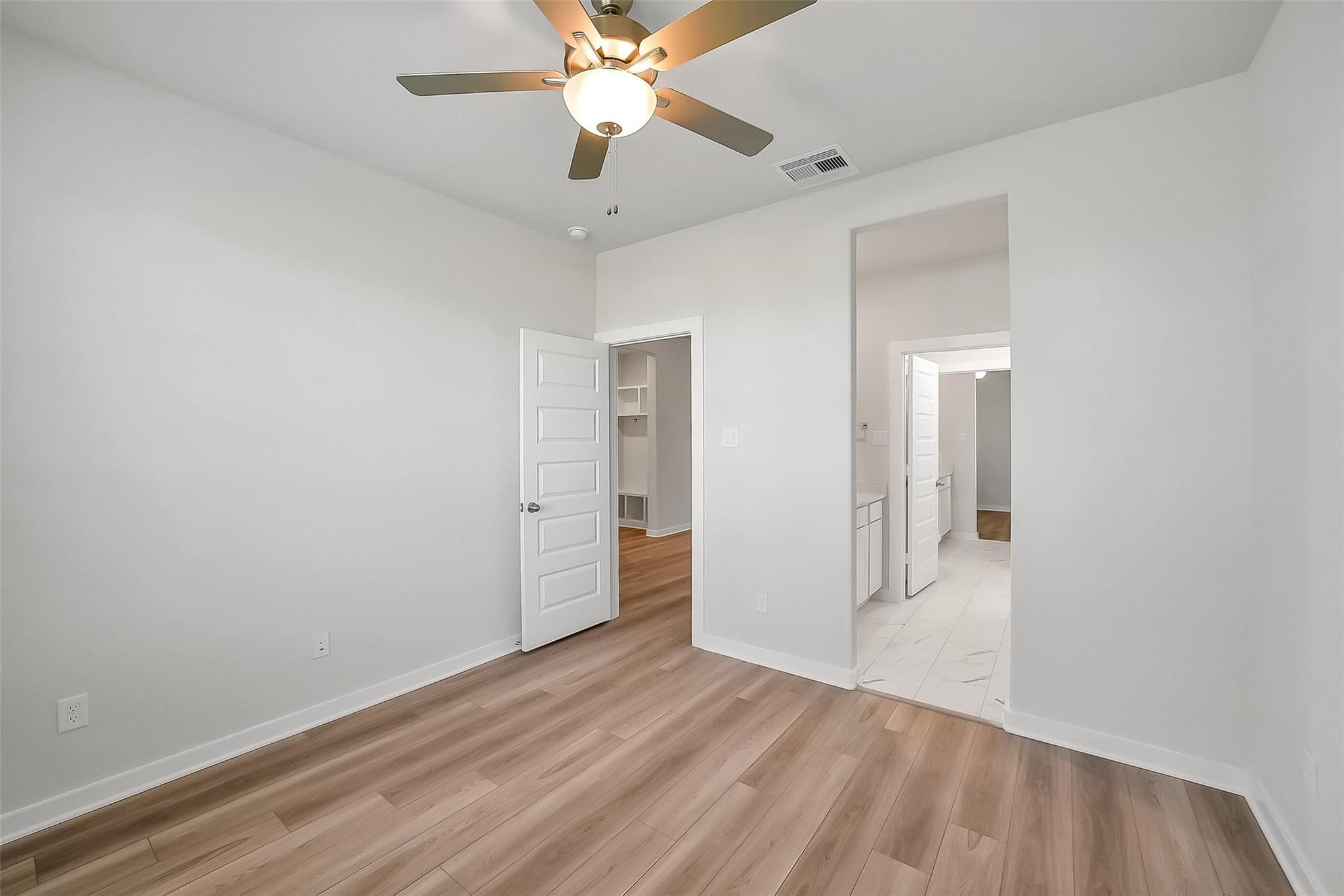 Bright secondary bedroom with ceiling fan, light wood floors, and en-suite bath in Davidson Homes The Acadia A, Sunterra, Katy, Texas