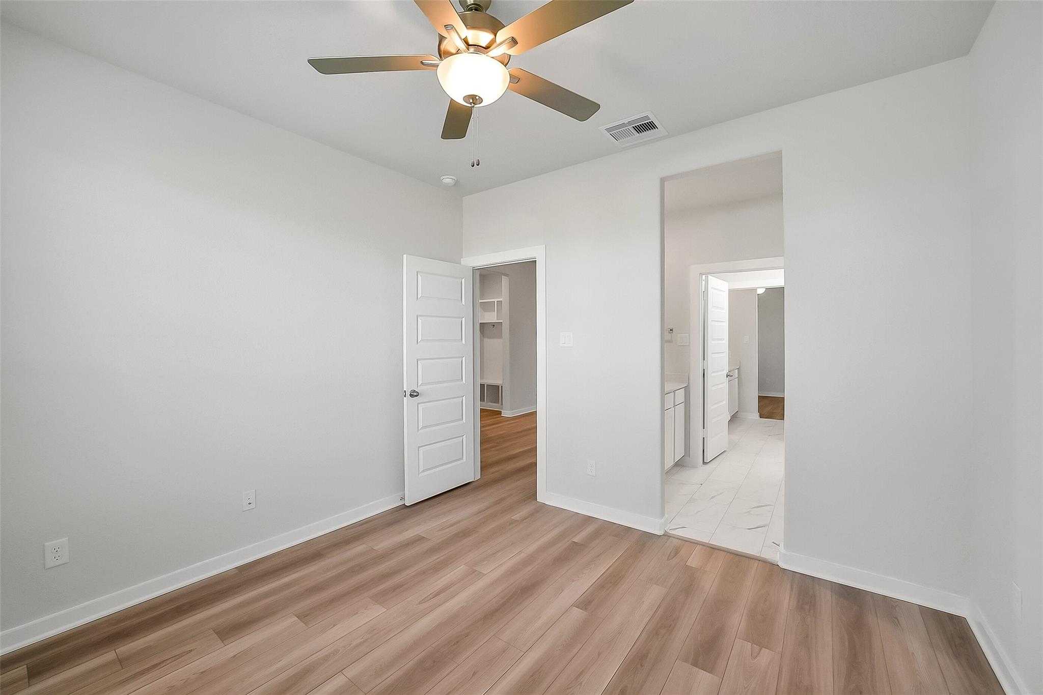 Bright secondary bedroom with ceiling fan, light wood floors, and en-suite bath in Davidson Homes The Acadia A, Sunterra, Katy, Texas