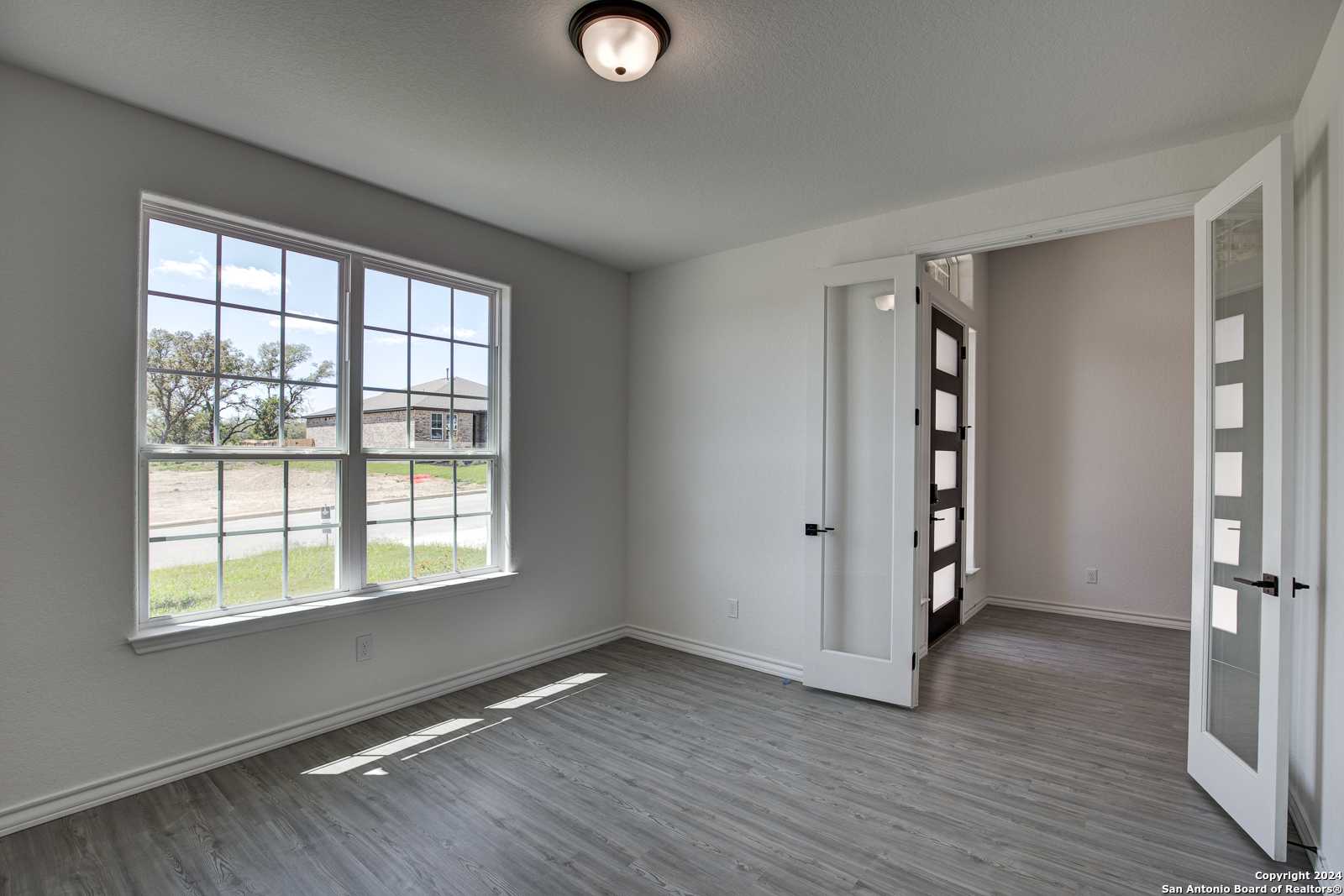 Sunlit study with large windows, gray walls, and open French doors in Davidson Homes The Garner B, Castroville Texas