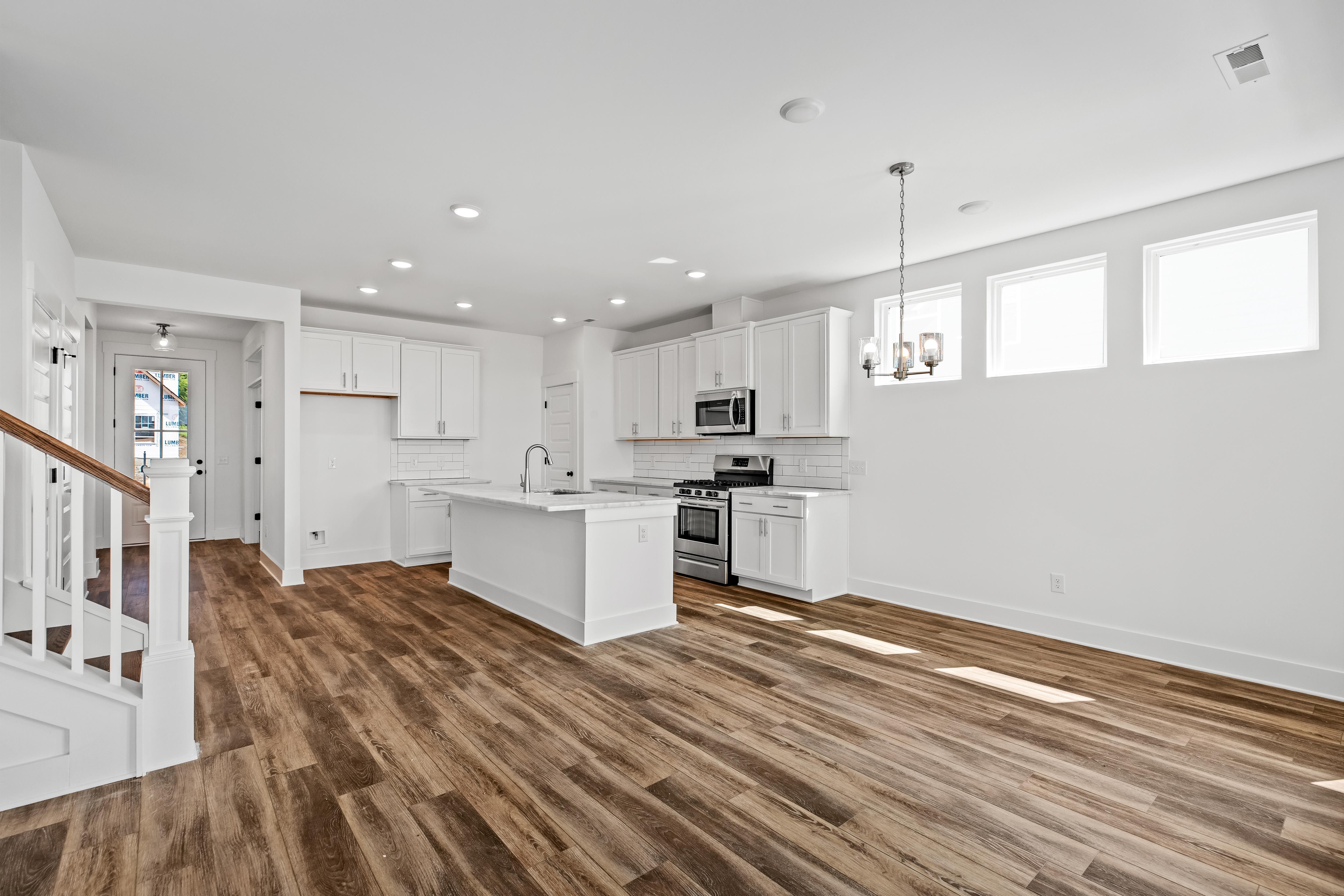 Open-concept kitchen in The Cedar D featuring white cabinetry, large center island, and wood-style flooring.