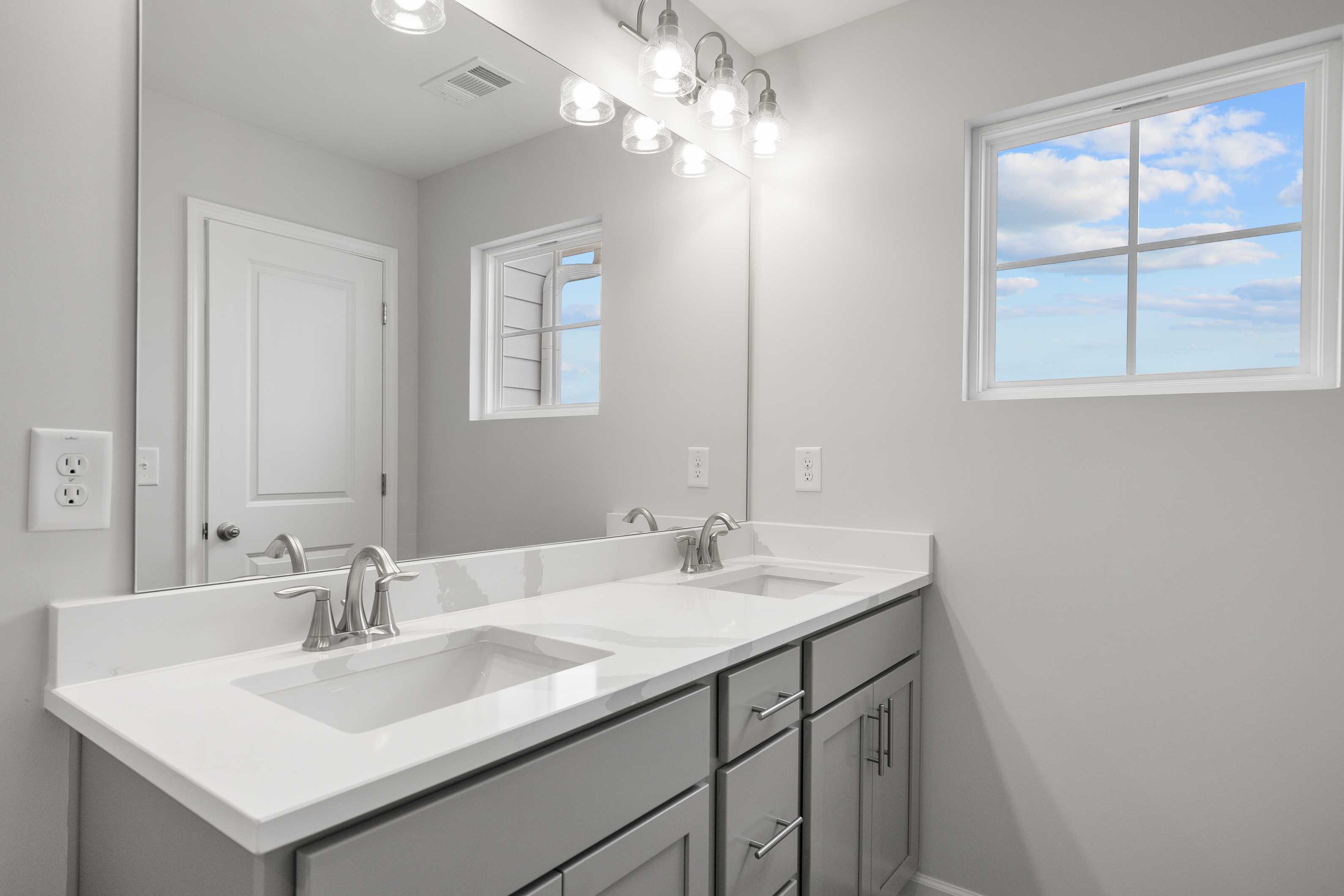 Spacious master bathroom in The Durant A with double vanity, gray shaker cabinets, large mirror, and window view