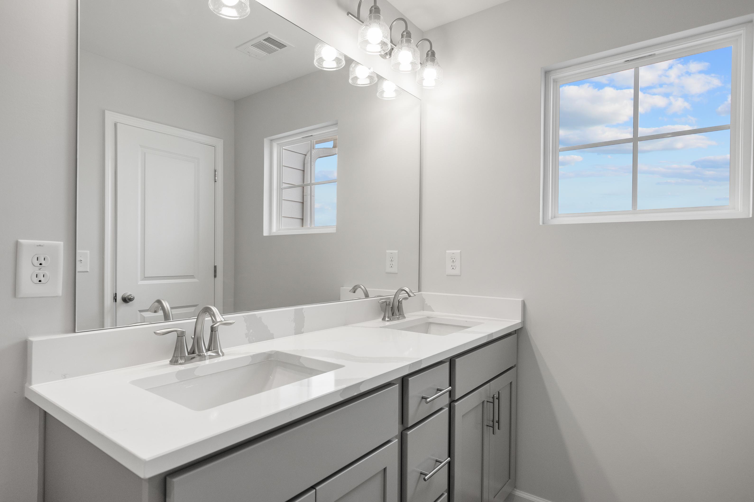 Spacious master bathroom in The Durant A with double vanity, gray shaker cabinets, large mirror, and window view