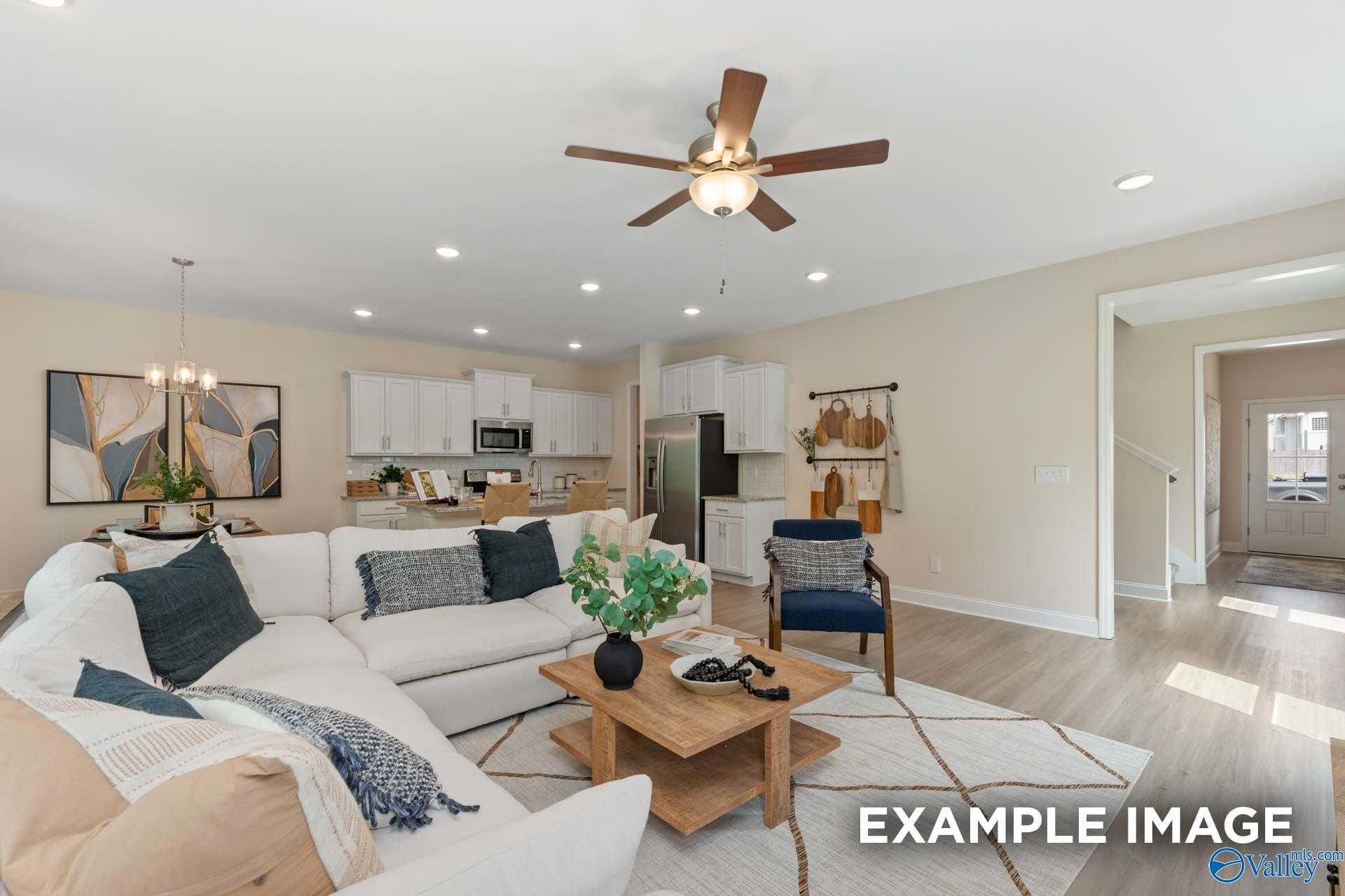 Inviting living room with L-shaped white sofa, ceiling fan, abstract wall art, and open kitchen in Davidson Homes The Camden B, Huntsville, Alabama