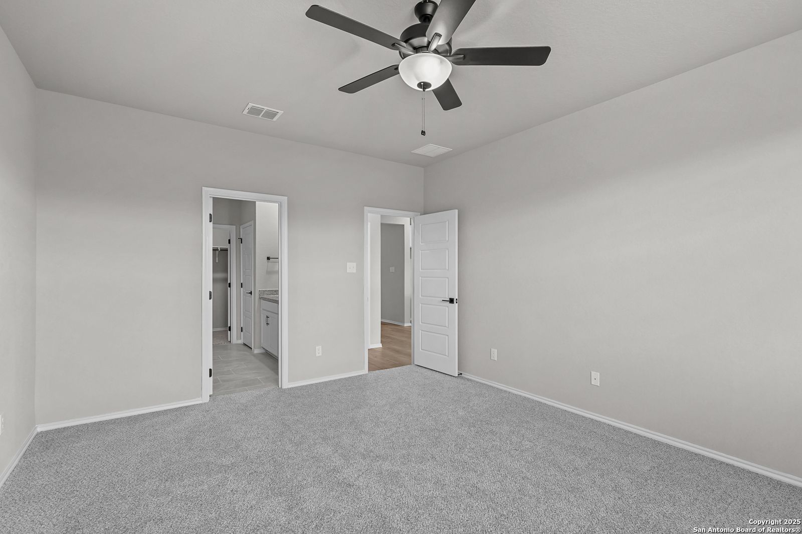 Spacious master bedroom with ceiling fan, gray walls, carpet flooring, and en-suite bath in Davidson Homes The Daphne K, San Antonio