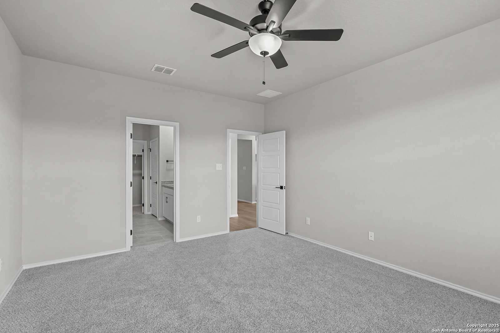 Spacious bedroom with gray carpet, walls, ceiling fan, adjacent bathroom and laundry in Davidson Homes The Daphne K, San Antonio