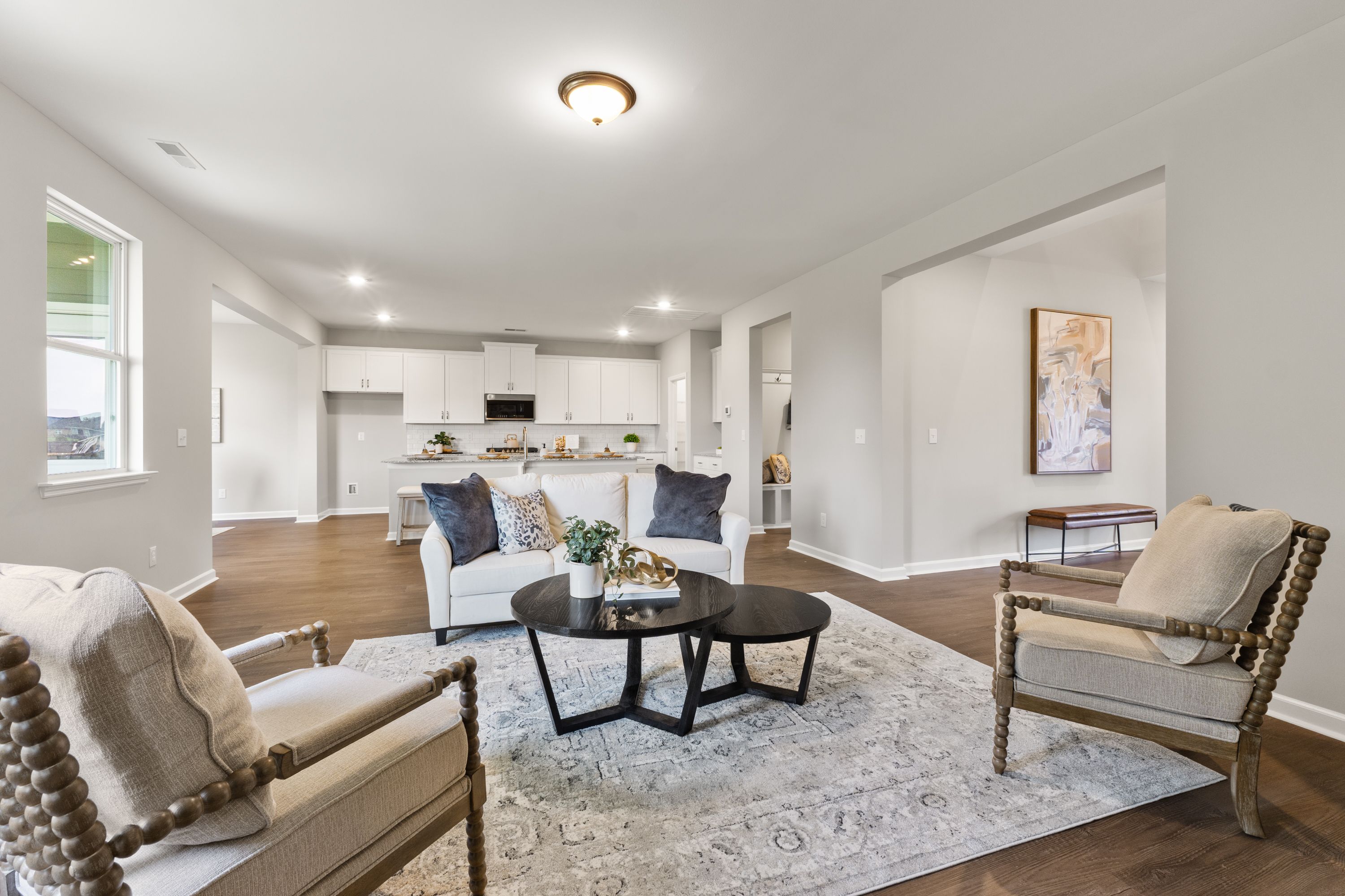 Spacious open-concept living room in The Avalon E with white sofa, modern kitchen cabinets, and beige armchairs on hardwood floors