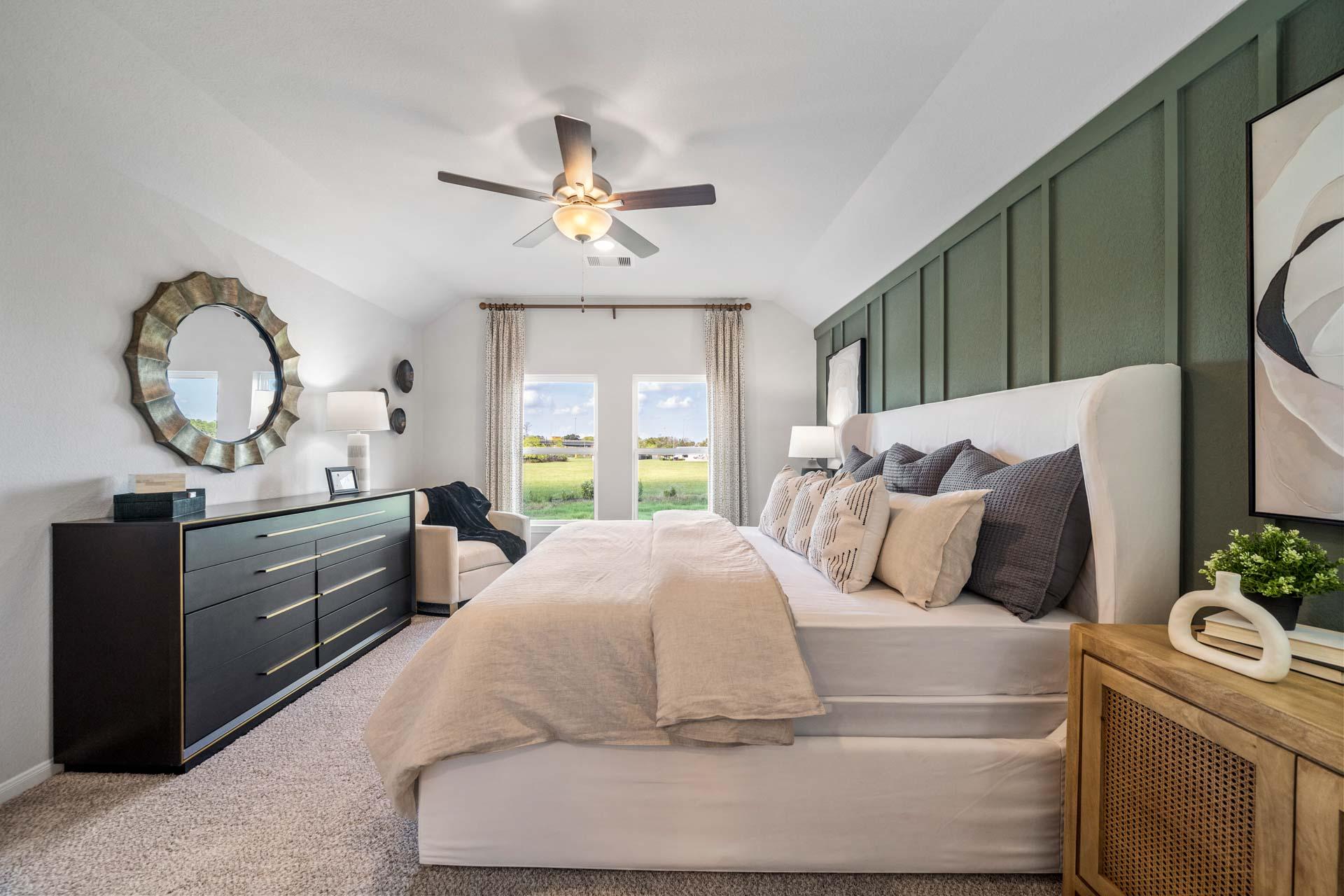 Spacious primary bedroom at Windmill Estates in Magnolia Texas with white tufted bed, green shiplap wall, and scenic field views